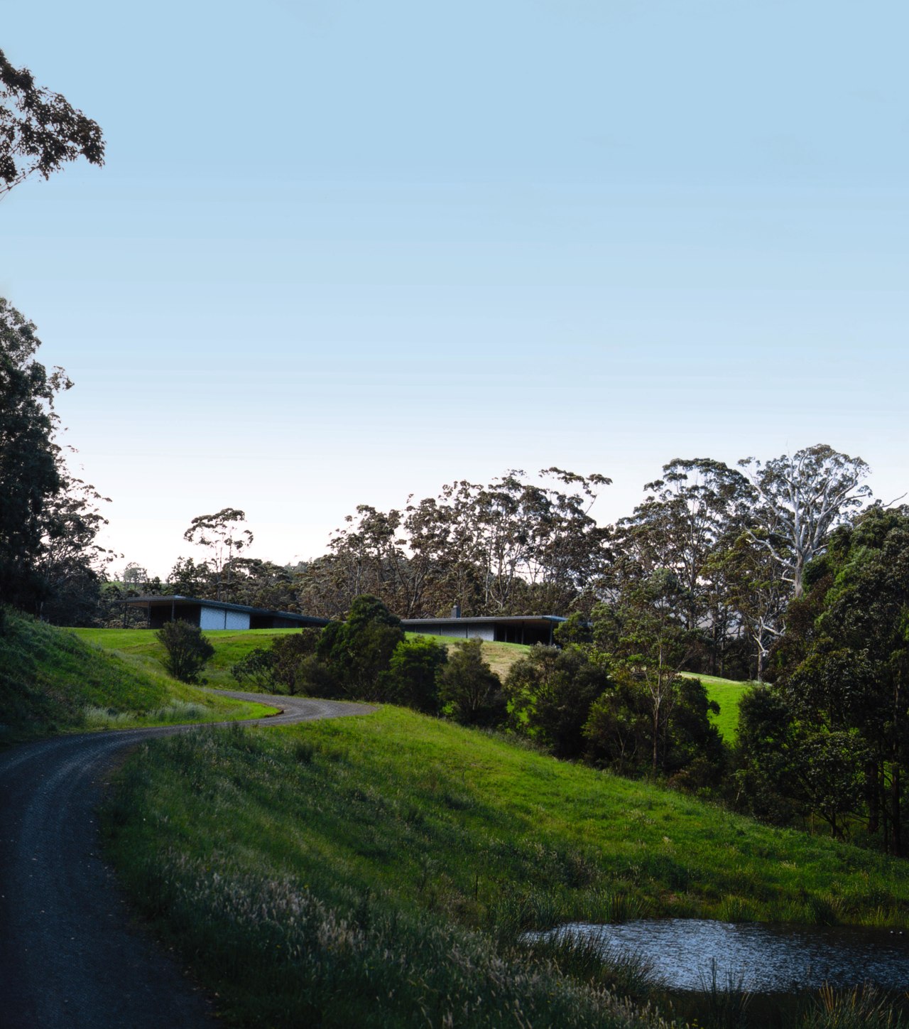 An exterior view of this architecturally designed home cloud, field, grass, green, highland, hill, landscape, leaf, meadow, morning, nature, plant, reflection, road, rural area, sky, sunlight, tree, vegetation, water, woody plant, white