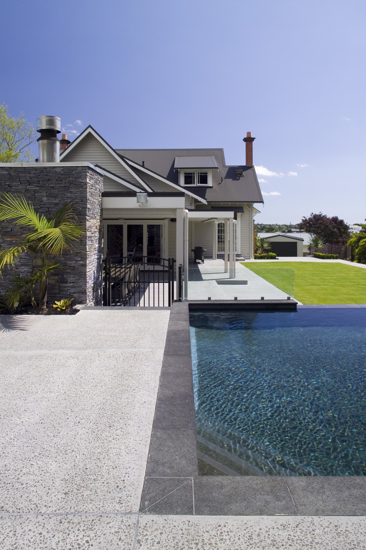 Stonework frames the pool and is also introduced architecture, backyard, cottage, driveway, estate, facade, home, house, landscaping, mansion, outdoor structure, property, real estate, residential area, roof, siding, sky, suburb, swimming pool, villa, walkway, water, window, teal