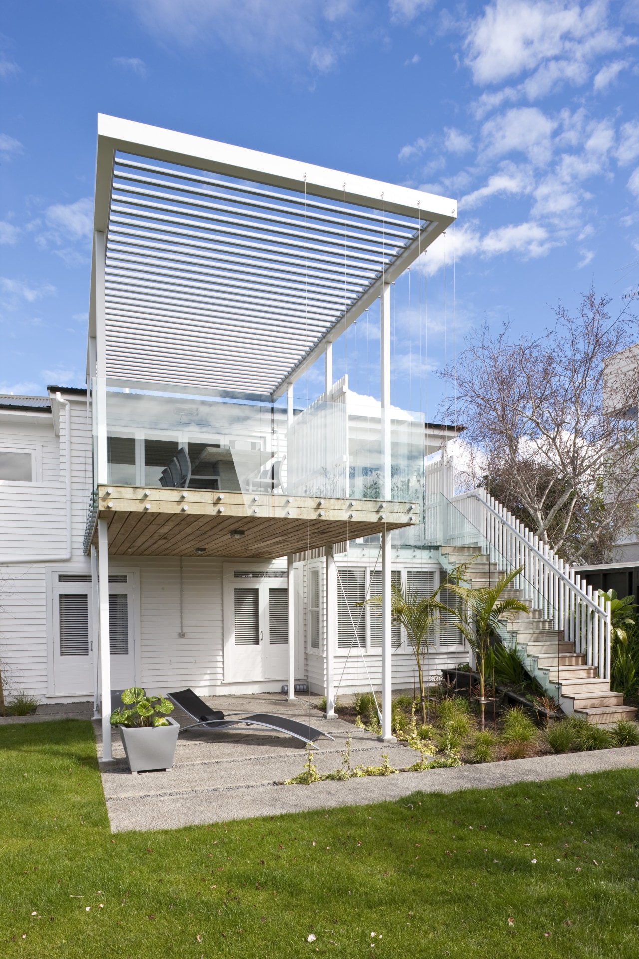 The renovated house features an elevated deck on architecture, corporate headquarters, daylighting, facade, home, house, outdoor structure, real estate, residential area, roof, white, teal