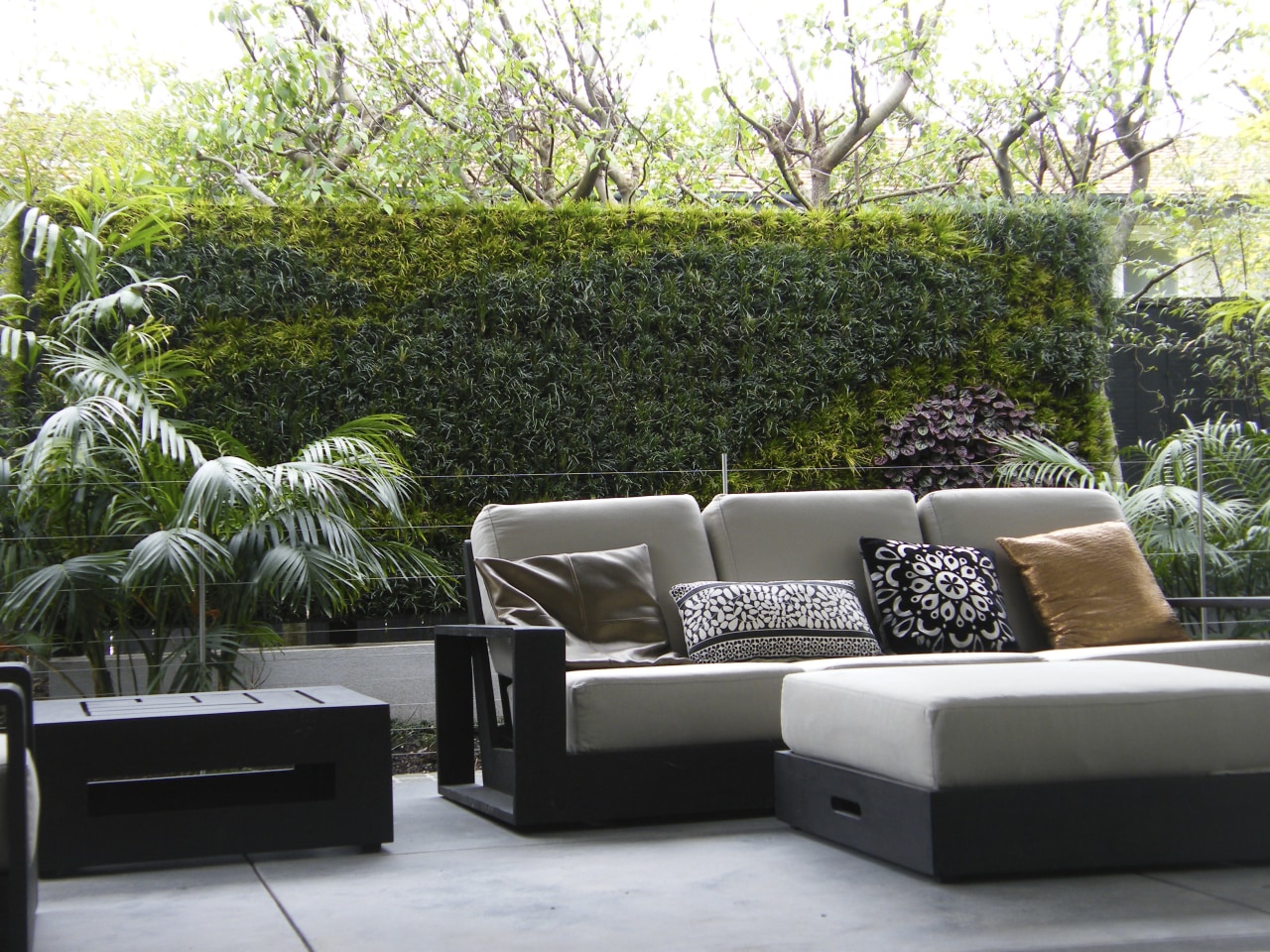 View of outdoor living space filled with mature couch, furniture, living room, outdoor furniture, outdoor structure, patio, table, wall