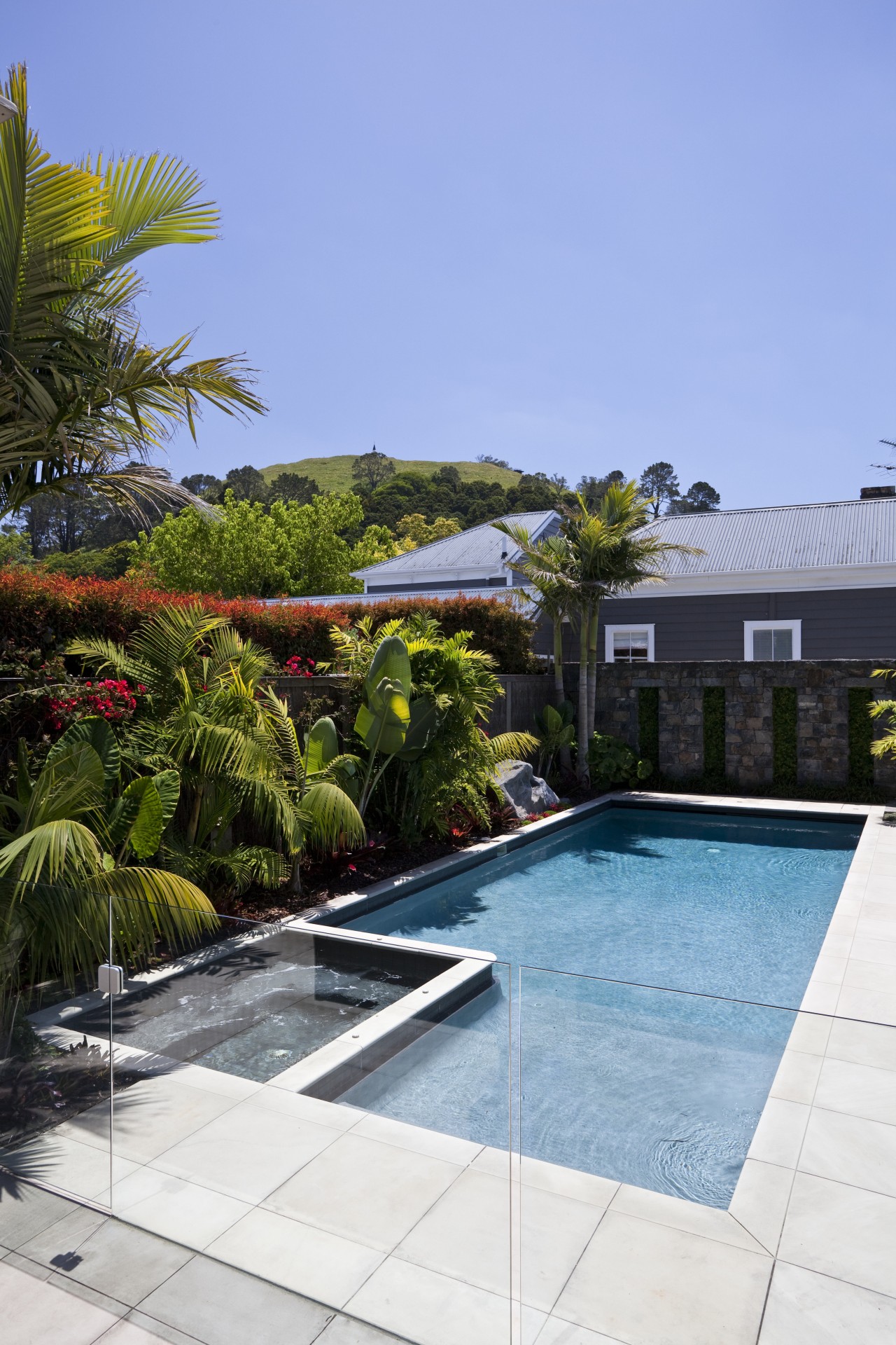 View of outdoor entertainment area, with pool, spa, architecture, arecales, backyard, estate, home, house, landscaping, leisure, palm tree, plant, property, real estate, residential area, resort, sky, swimming pool, tree, vacation, villa, water, teal