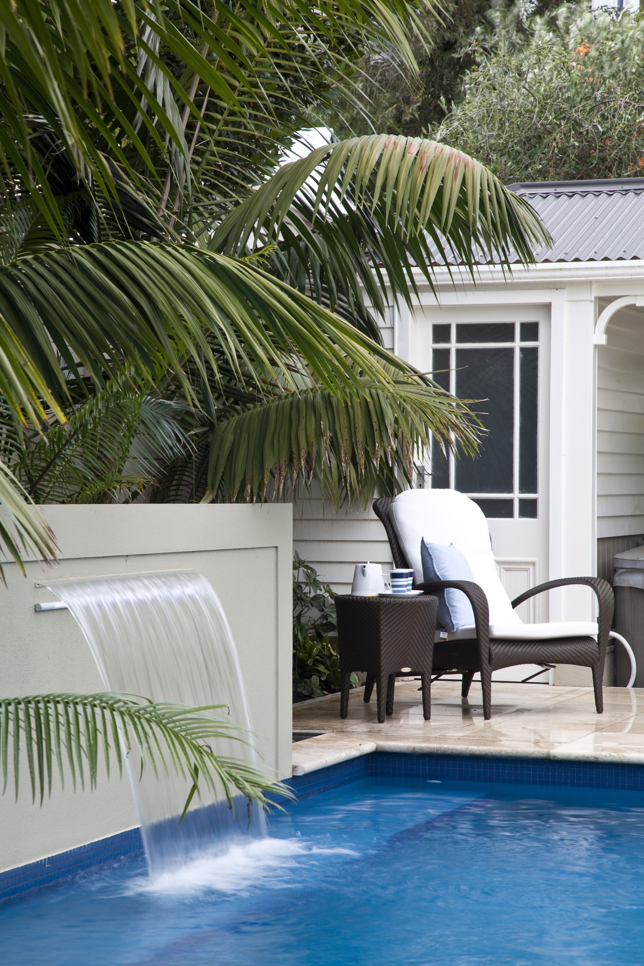 View of outdoor area with pool, paving, fountain, arecales, backyard, estate, home, house, outdoor furniture, outdoor structure, palm tree, plant, property, real estate, resort, sunlounger, swimming pool, tree, water, window, gray