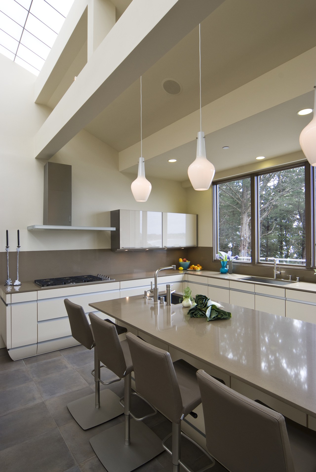 View of neutral-toned kitchen and dining space, featuring architecture, ceiling, countertop, daylighting, floor, house, interior design, kitchen, real estate, table, gray