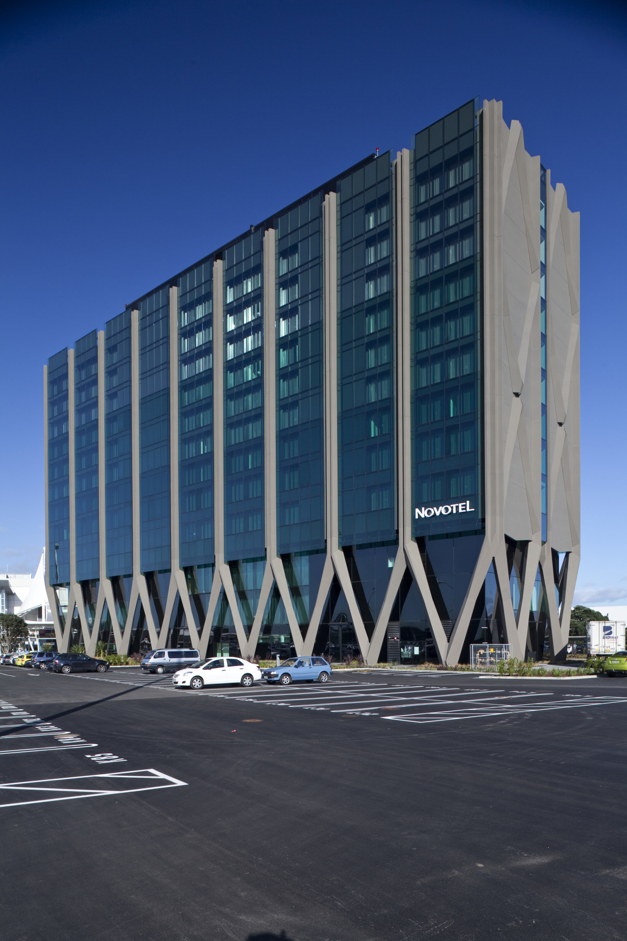 The Novotel Auckland Airport hotel's intricate concrete structure architecture, building, commercial building, condominium, corporate headquarters, daytime, facade, headquarters, landmark, metropolis, metropolitan area, sky, structure, tower block, urban area, blue, black