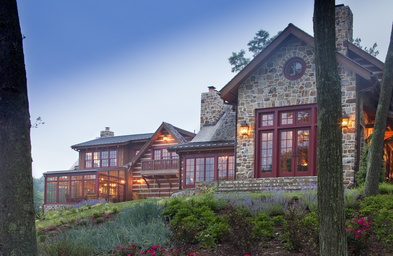 View of stone building with red window frames. building, cottage, estate, evening, facade, farmhouse, home, house, mansion, property, real estate, residential area, roof, sky, tree, window, teal