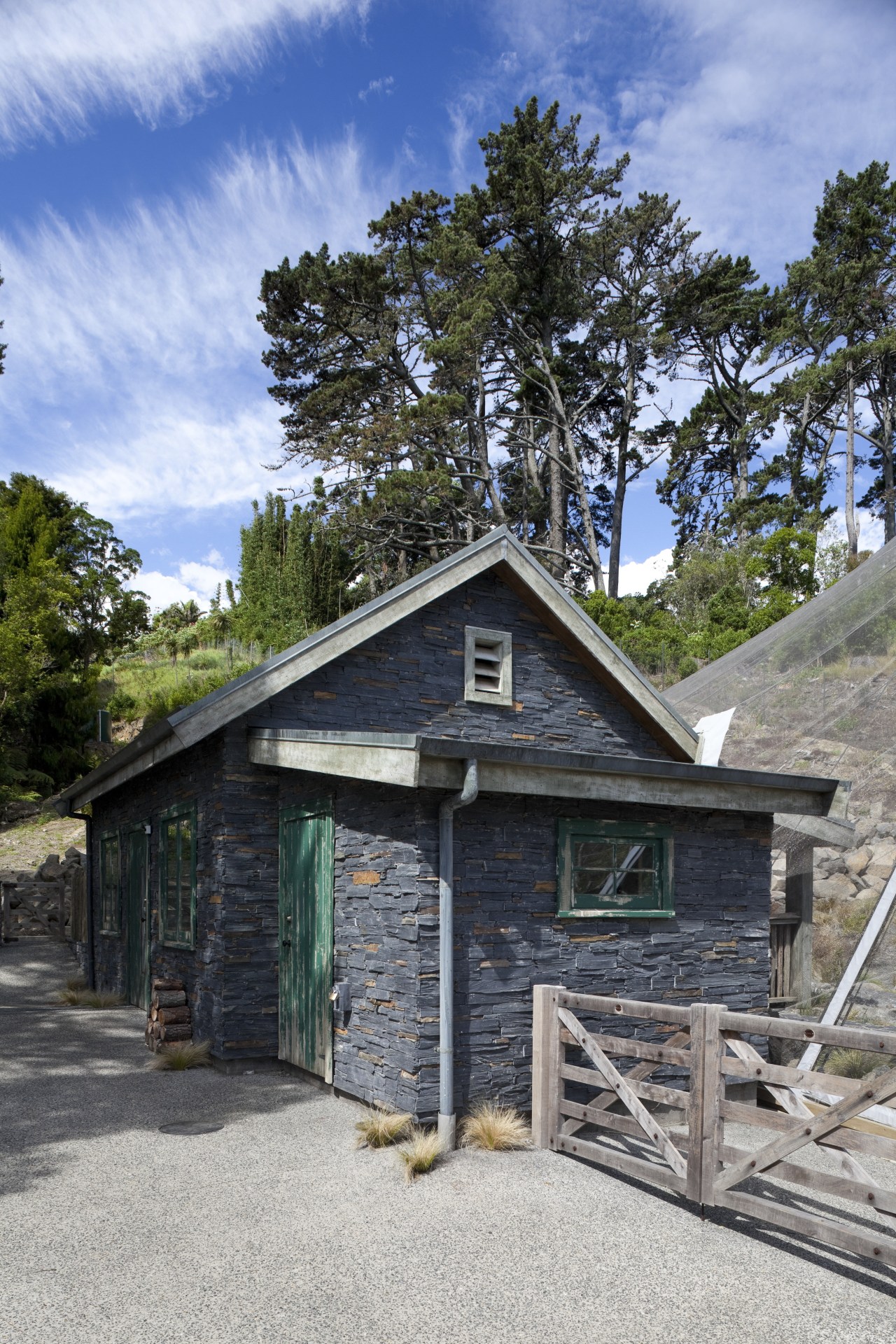 Exterior view of stone building with wooden fence. cottage, farmhouse, home, house, hut, log cabin, property, real estate, shack, shed, sky, tree, wood, gray, teal, black