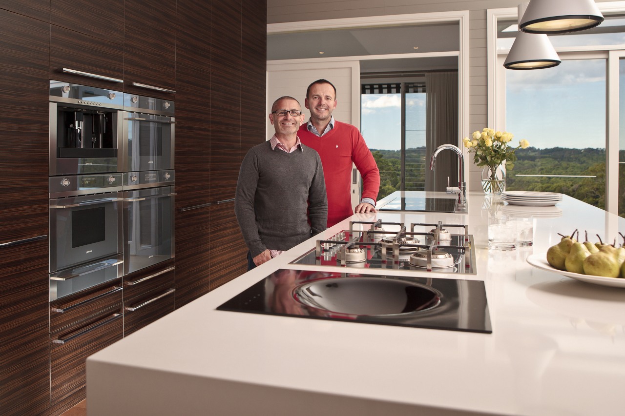 Two men in a kitchen with brown wooden countertop, home appliance, interior design, kitchen, kitchen appliance, white, red