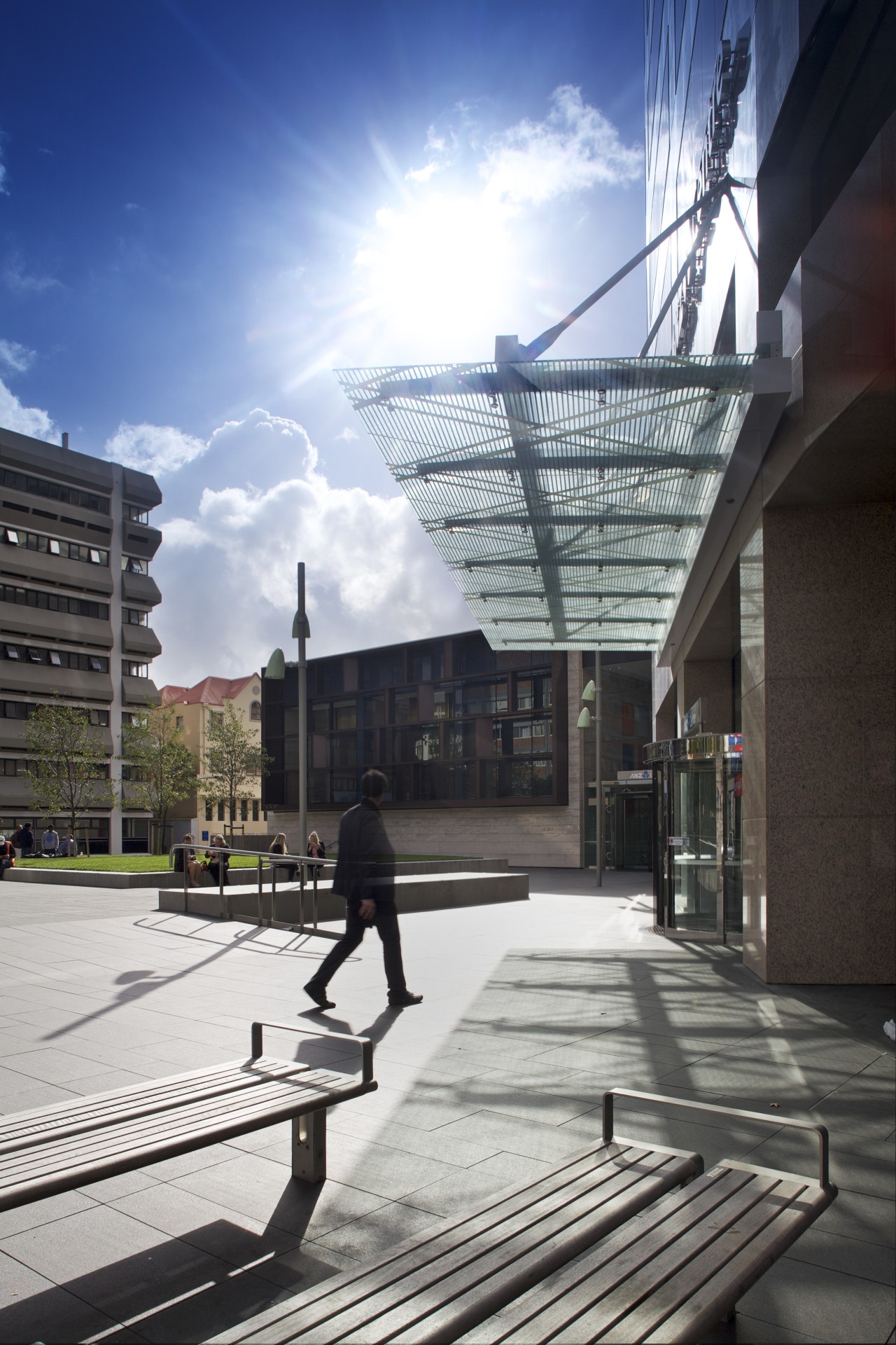 Sleek glass canopies replace the heavy rosso porrino architecture, building, city, cloud, daytime, facade, infrastructure, metropolitan area, mixed use, reflection, residential area, sky, sunlight, town, urban area, urban design, walkway, black, white