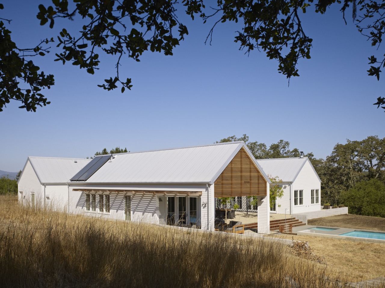 The gabled volumes in this country house reference barn, cottage, estate, farm, farmhouse, home, house, property, real estate, residential area, roof, rural area, sky, teal, brown