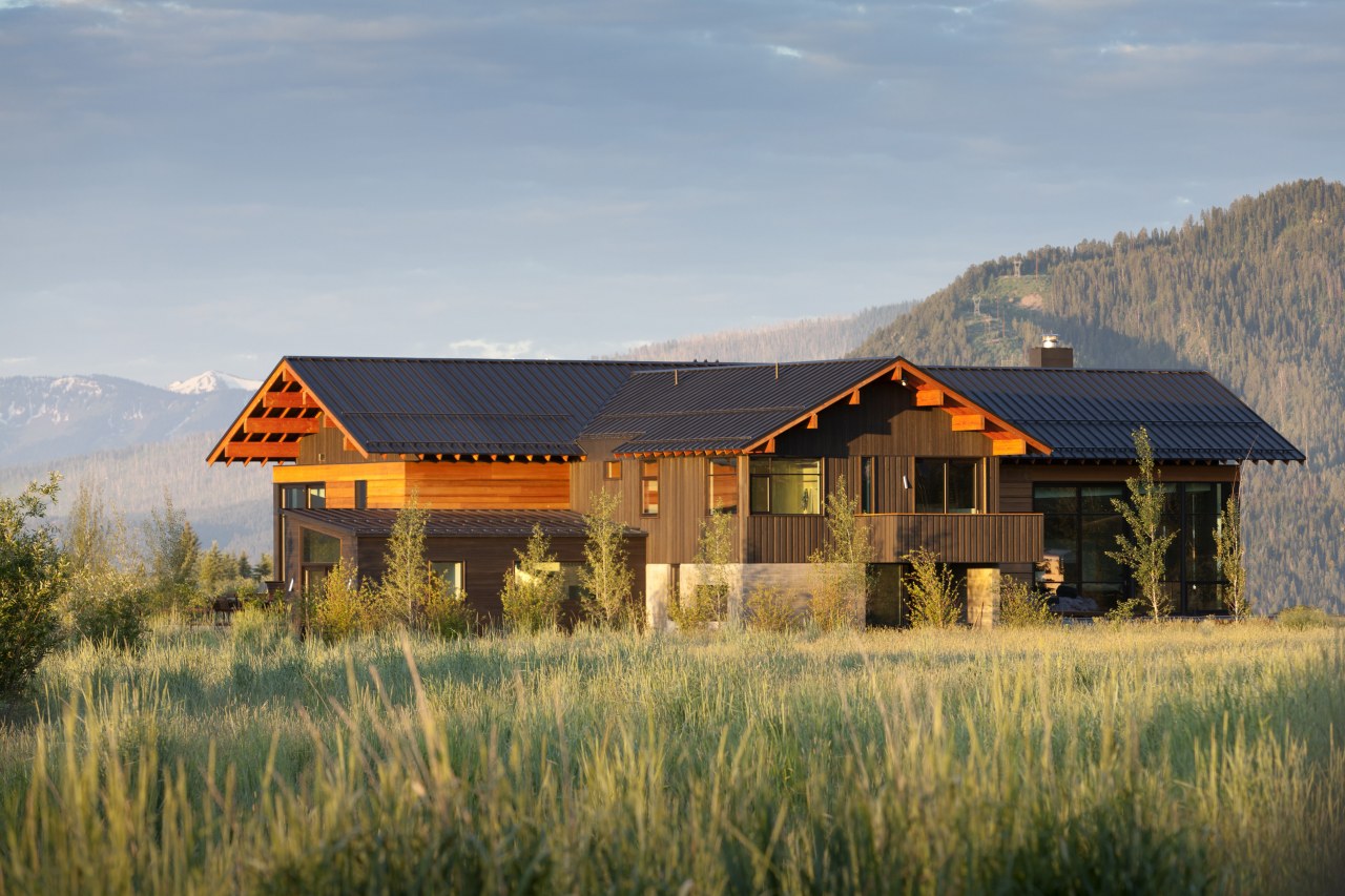 This rustic-looking mountain home features a central living cottage, estate, farm, farmhouse, field, grass, grassland, home, house, hut, landscape, log cabin, mountain, property, ranch, real estate, rural area, sky, gray, brown