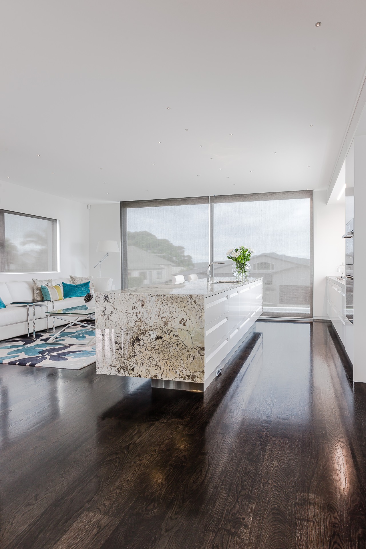 A textural granite benchtop with waterfall ends wraps apartment, architecture, ceiling, daylighting, floor, flooring, hardwood, home, house, interior design, laminate flooring, living room, wood, wood flooring, gray