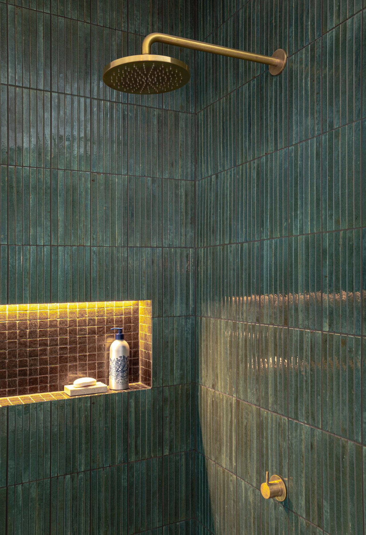 The back-lit shower niche illuminates the brass shower 
