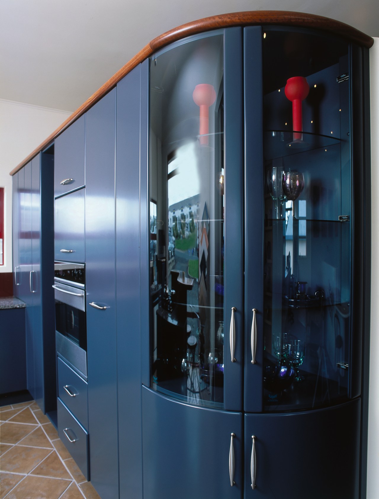 Kitchen with tall blue coloured cabinetry, wall oven cabinetry, display case, glass, black