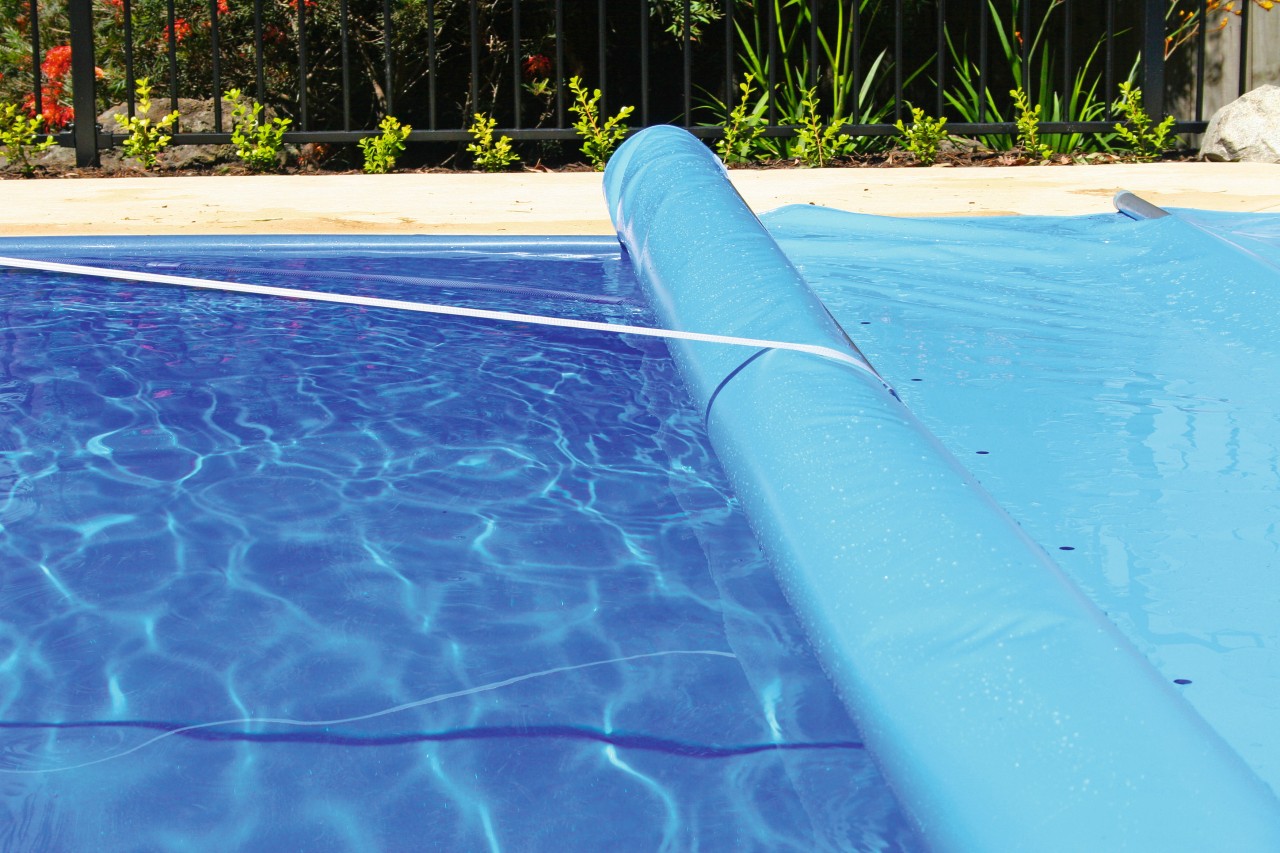 Swimming pool with blue cover being rolled up. azure, blue, leisure, swimming pool, water, teal, blue