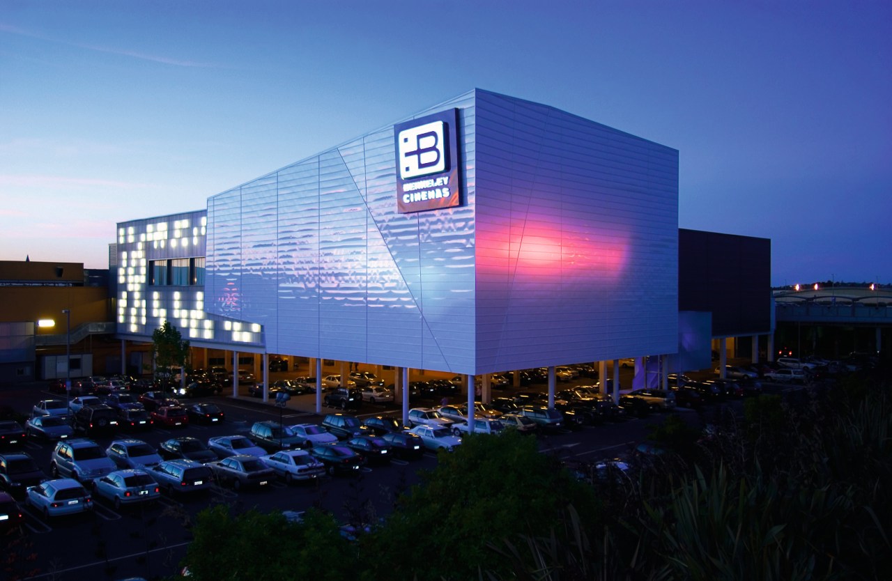 Evening view of Berkeley cinema complex with angular architecture, building, convention center, corporate headquarters, display device, facade, headquarters, metropolitan area, mixed use, night, reflection, sky, structure, blue, black