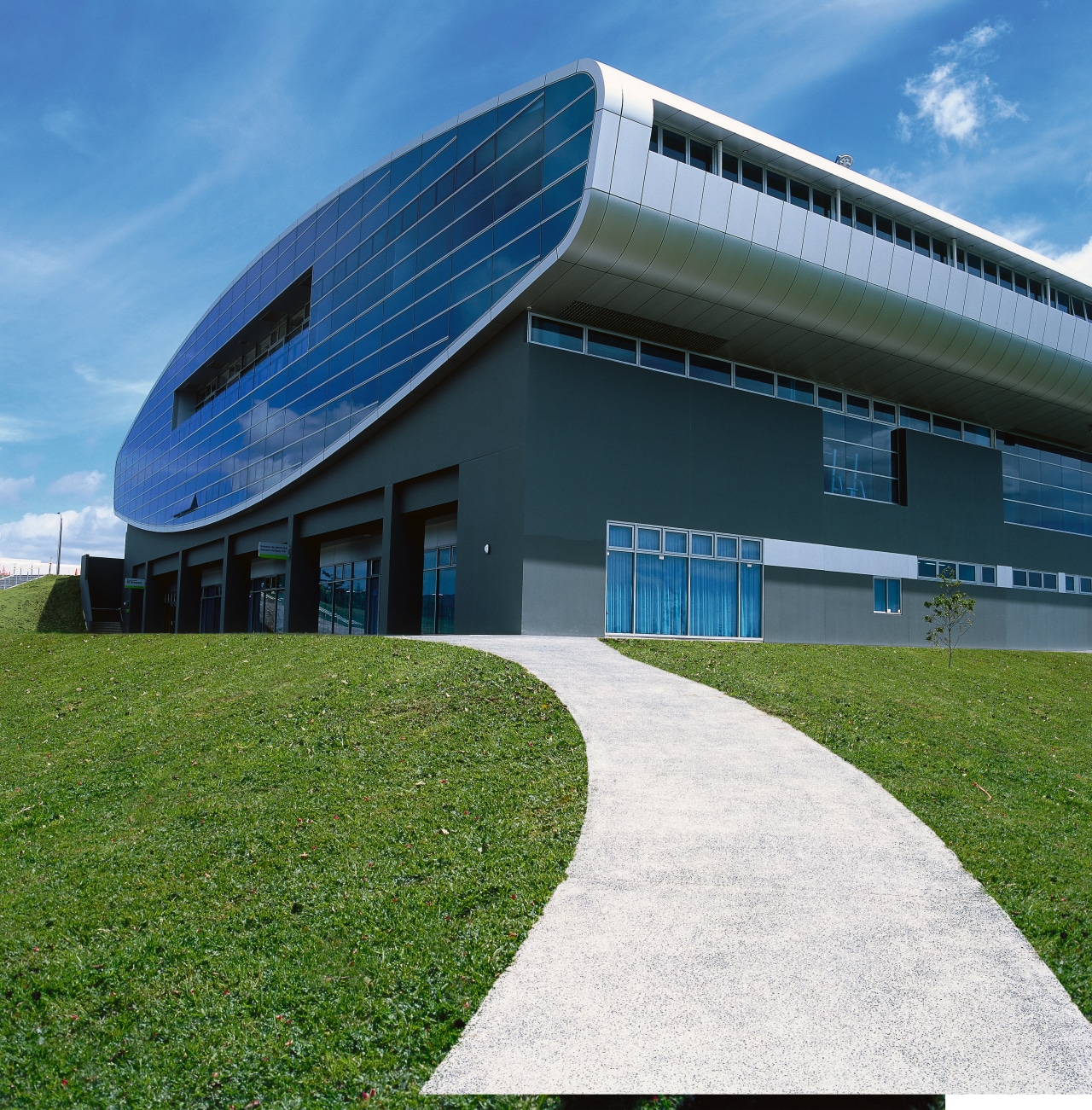 Exterior view of grey concrete clad stadium building architecture, building, corporate headquarters, daytime, facade, grass, headquarters, house, real estate, sky, structure, teal