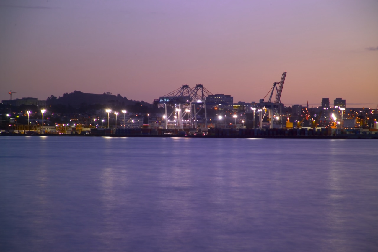 Distant view of Port of Auckland complex, showing body of water, calm, city, cityscape, dawn, downtown, dusk, evening, horizon, night, reflection, river, sea, sky, skyline, sunset, water, waterway, purple