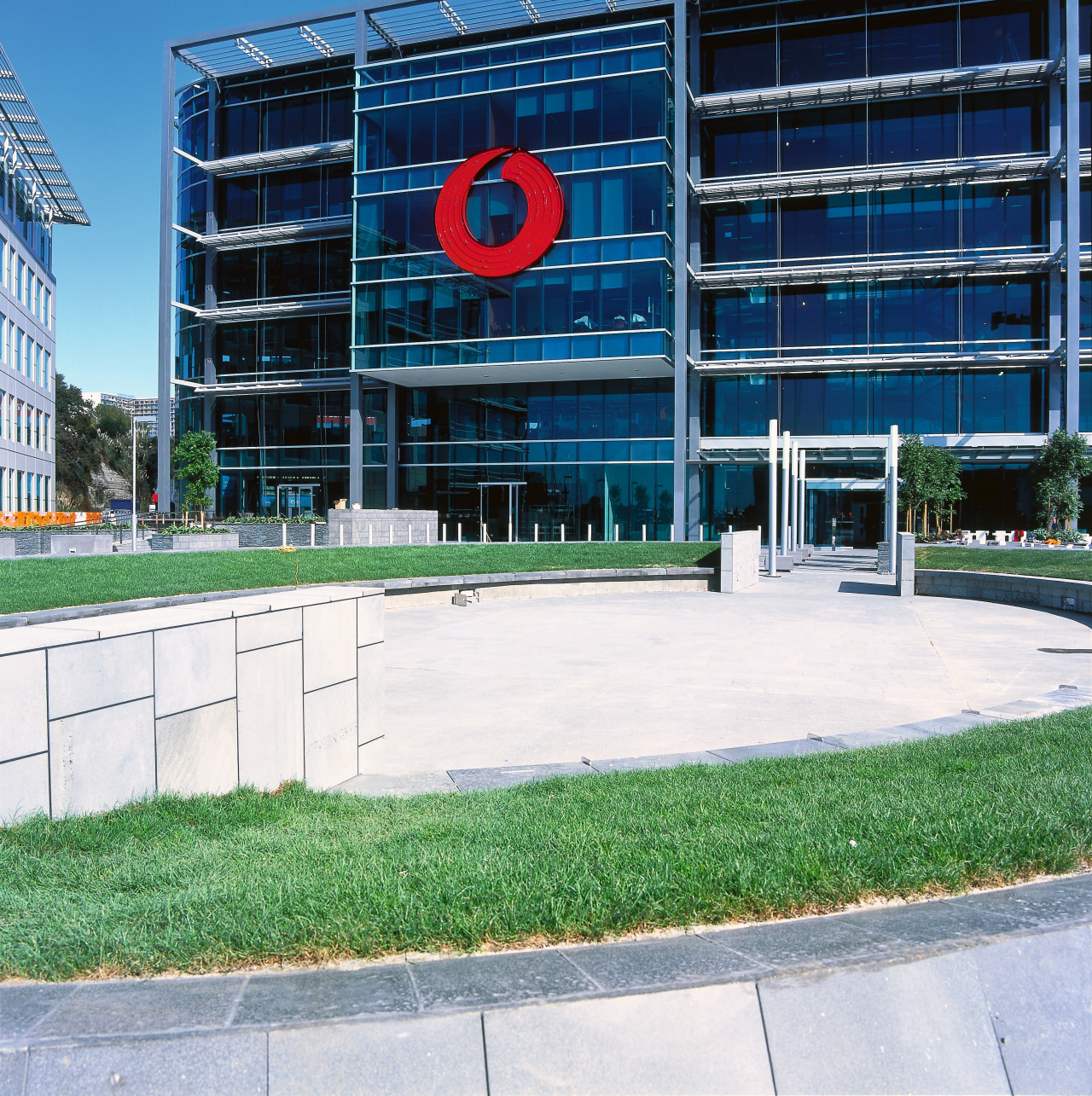View of front of Vodafone building with grass architecture, building, city, condominium, corporate headquarters, daytime, facade, grass, headquarters, neighbourhood, real estate, residential area, sky, urban area, white
