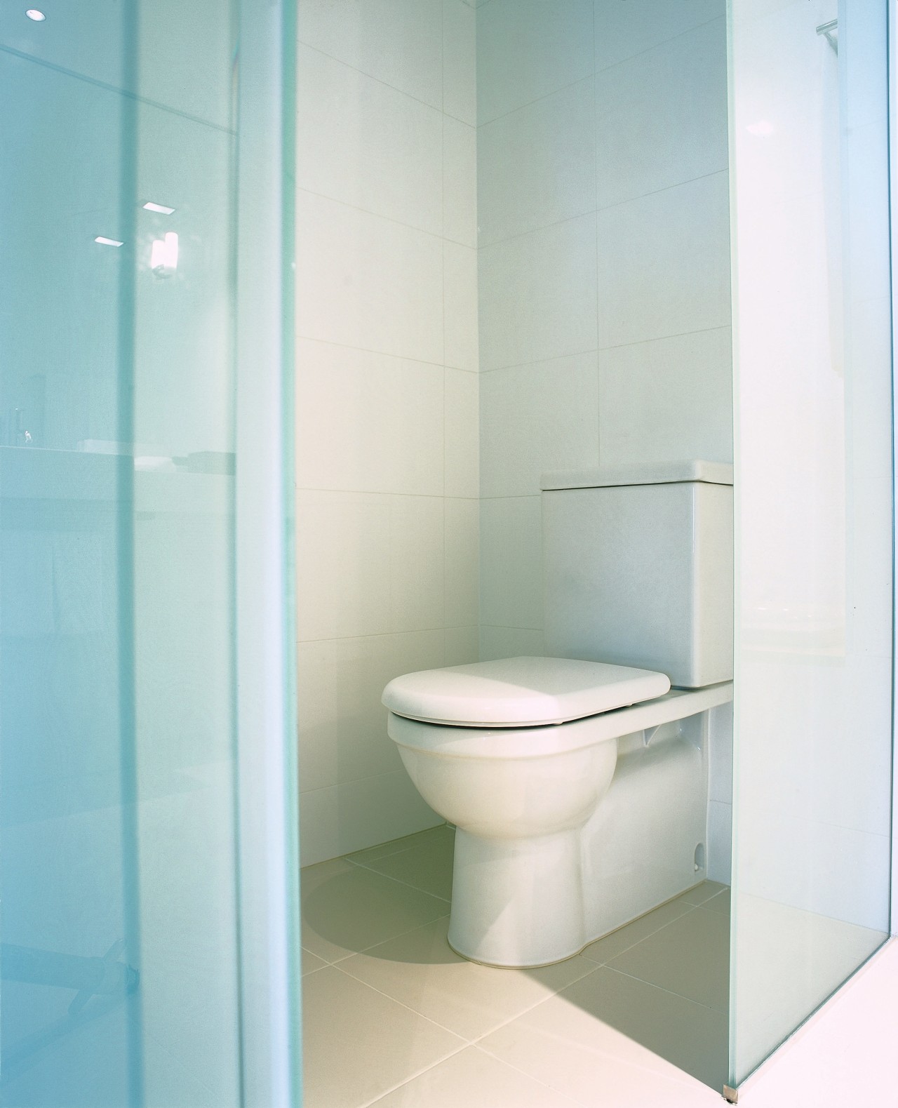 View of white toilet in small room. bathroom, bathroom accessory, bathroom cabinet, bathroom sink, bidet, ceramic, plumbing fixture, product design, tap, tile, toilet, toilet seat, white