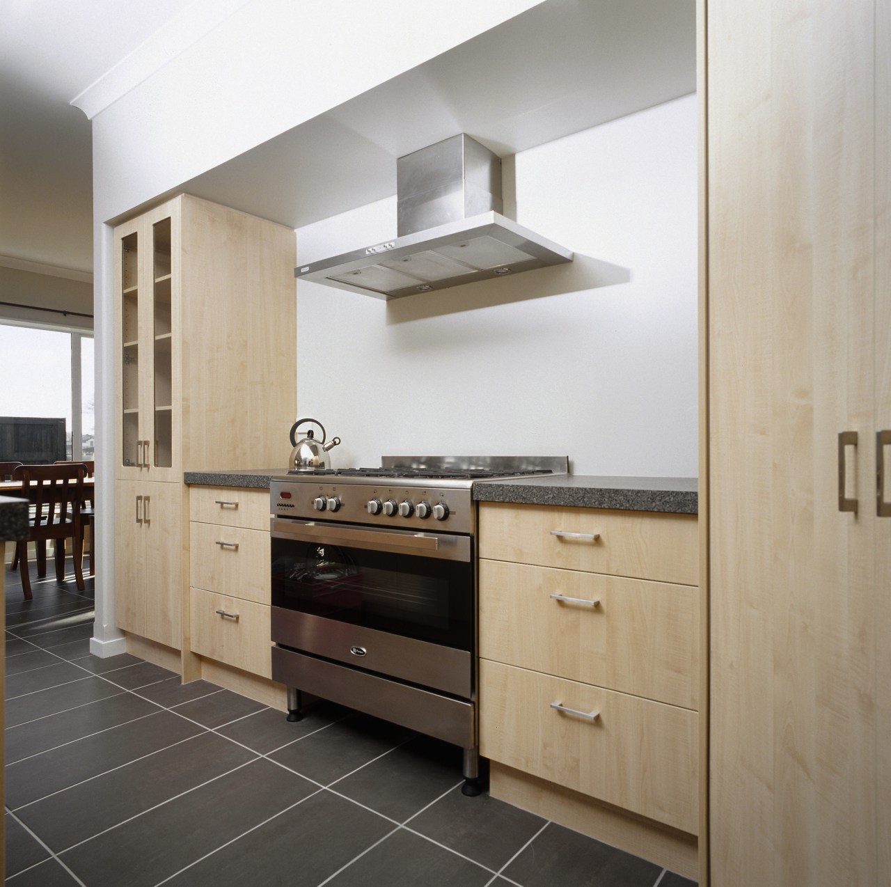 Kitchen with light tan cabinetry, stainless steel oven cabinetry, countertop, cuisine classique, floor, furniture, home appliance, interior design, kitchen, room, gray