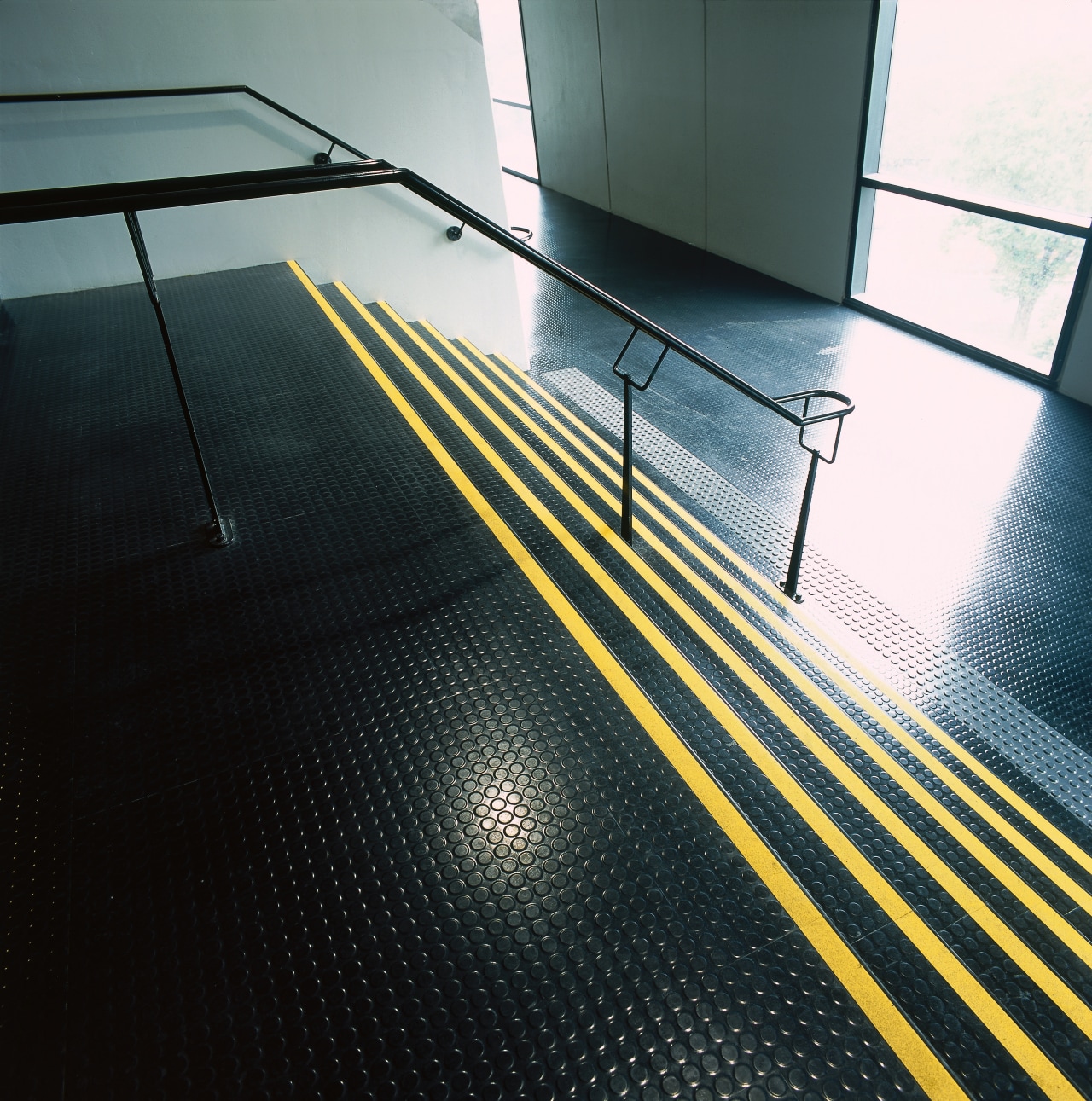 View of stairwell with black studded rubber flooring, angle, architecture, daylighting, floor, flooring, glass, hardwood, light, lighting, line, structure, sunlight, wood, yellow, black