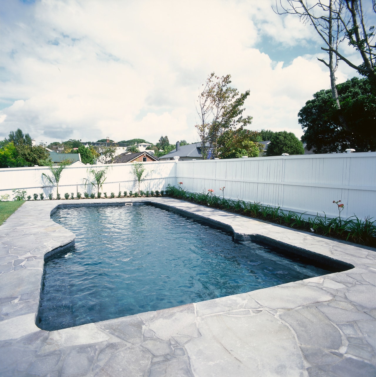 A view of a swimming pool. backyard, estate, fence, leisure, outdoor structure, property, real estate, swimming pool, wall, water, white, gray