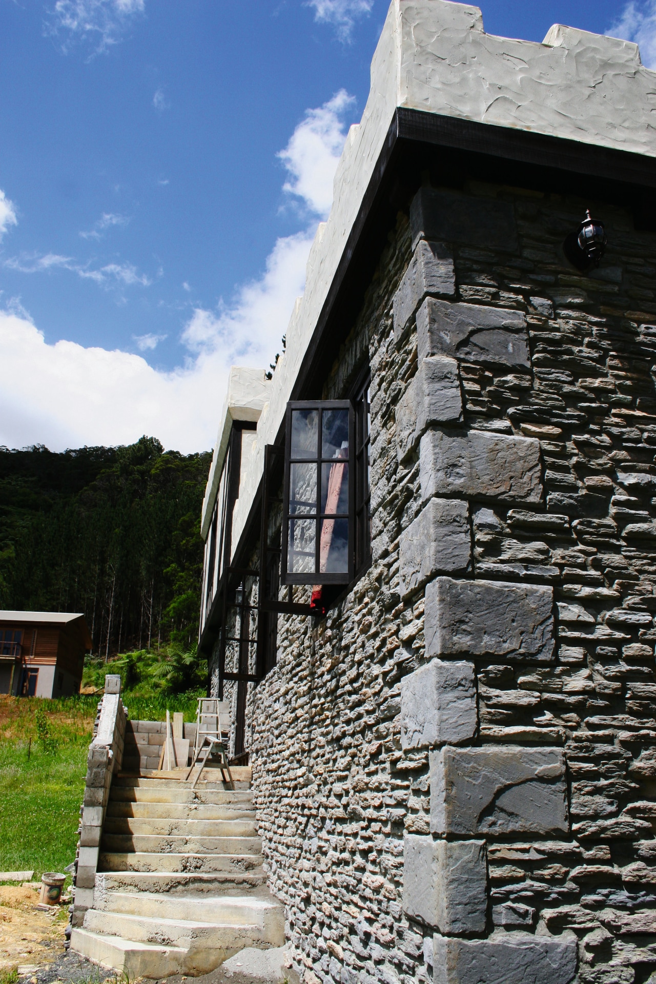 View of exterior of home clad in stone. building, cottage, facade, house, sky, stone wall, wall, window, black, gray