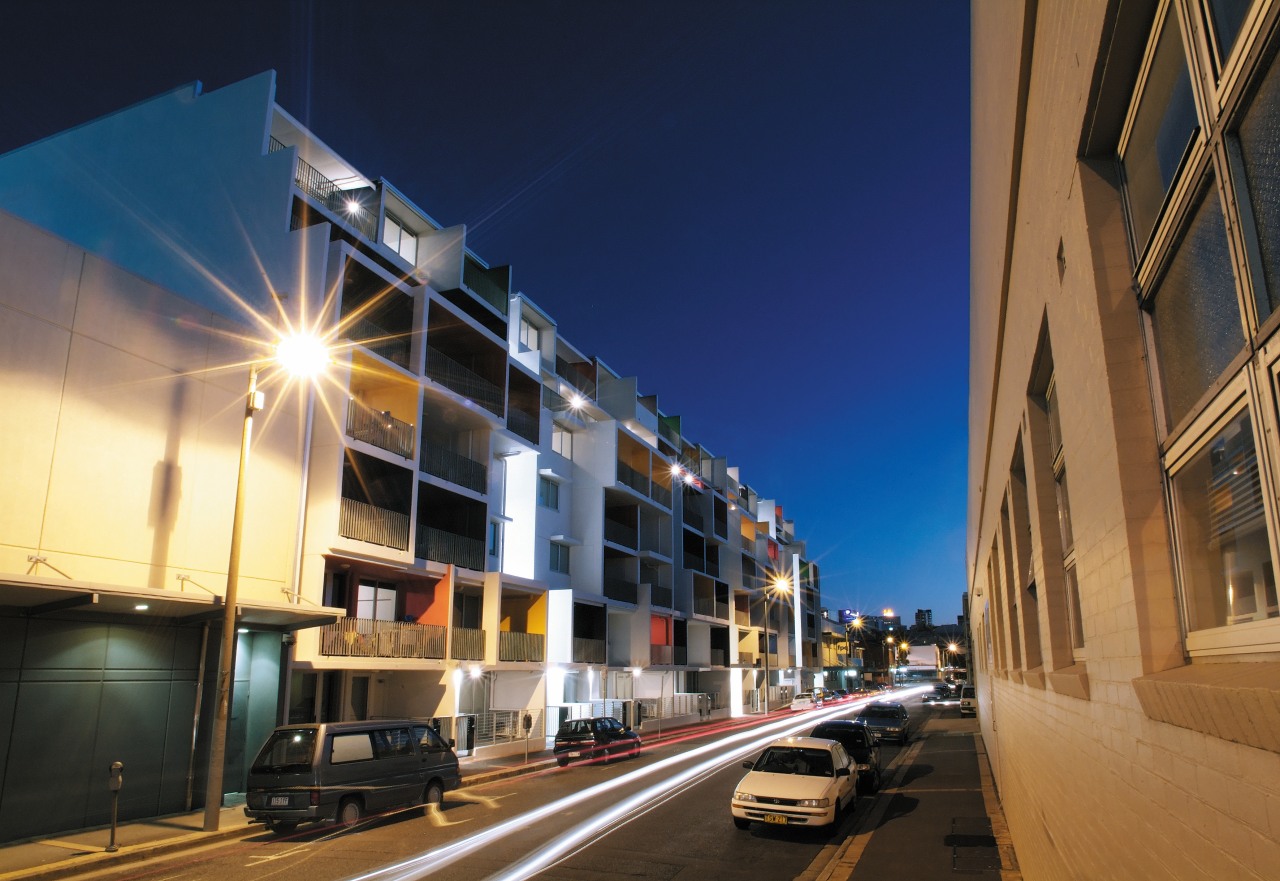 Exterior view of this new apartment development featuring apartment, architecture, building, car, city, commercial building, condominium, downtown, evening, facade, infrastructure, lighting, metropolis, metropolitan area, mixed use, neighbourhood, night, real estate, residential area, road, sky, street, town, urban area, blue