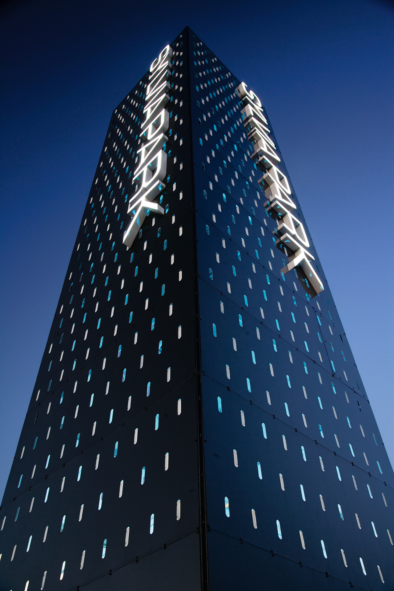 A view of some signage by Corada. architecture, building, commercial building, corporate headquarters, daytime, facade, landmark, metropolis, metropolitan area, sky, skyscraper, tower, tower block, blue, black