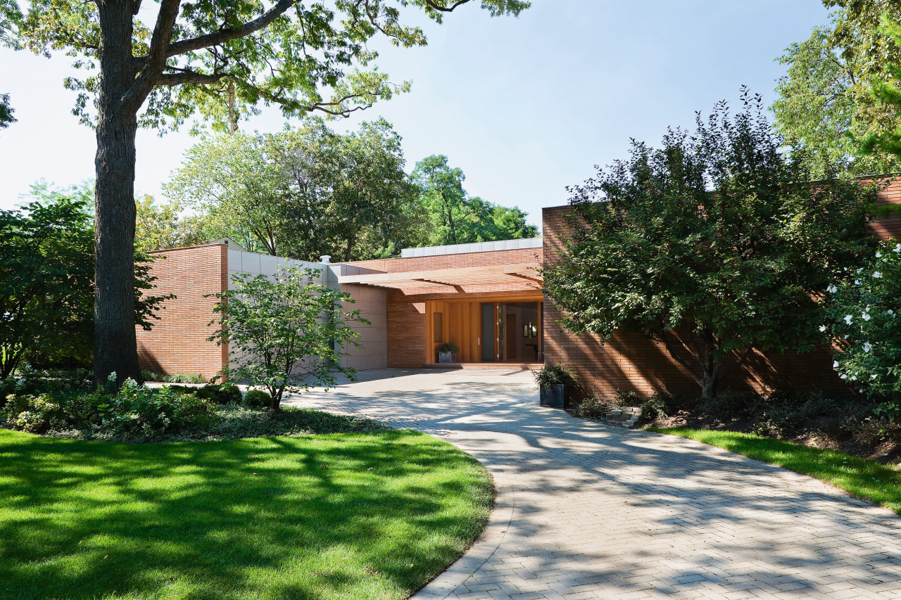 An exterior view of the entrance way to backyard, cottage, courtyard, estate, facade, garden, grass, home, house, landscape, landscaping, outdoor structure, property, real estate, residential area, tree, villa, walkway, yard, white, green