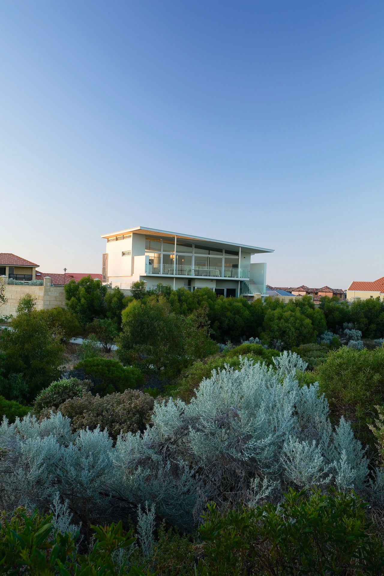 Exterior view of this beach house nestled amongst architecture, city, estate, home, house, landscape, neighbourhood, plant, property, real estate, residential area, sky, suburb, tree, villa, teal