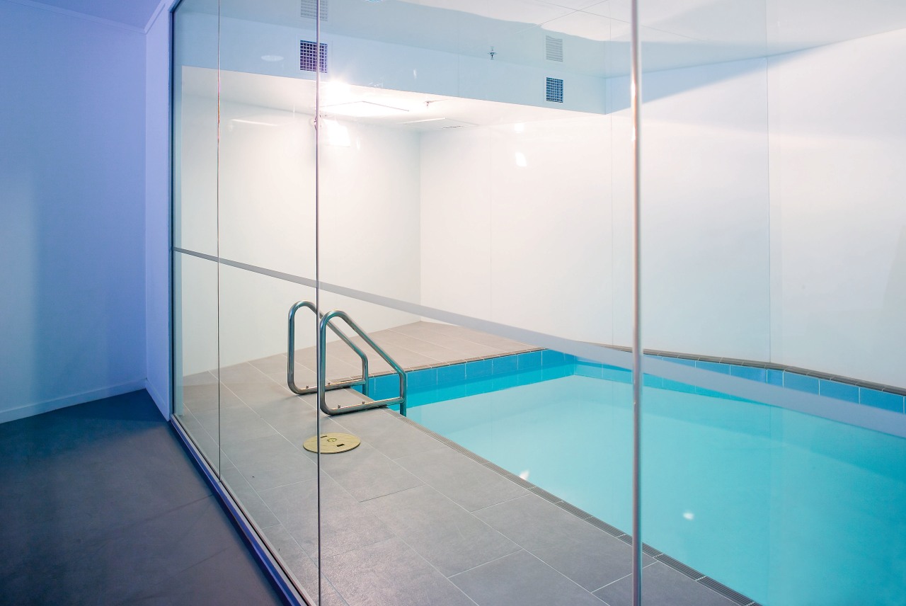 A view of a swimming pool featuring a architecture, bathroom, ceiling, floor, flooring, glass, interior design, leisure centre, lighting, room, tile, wall, white, teal