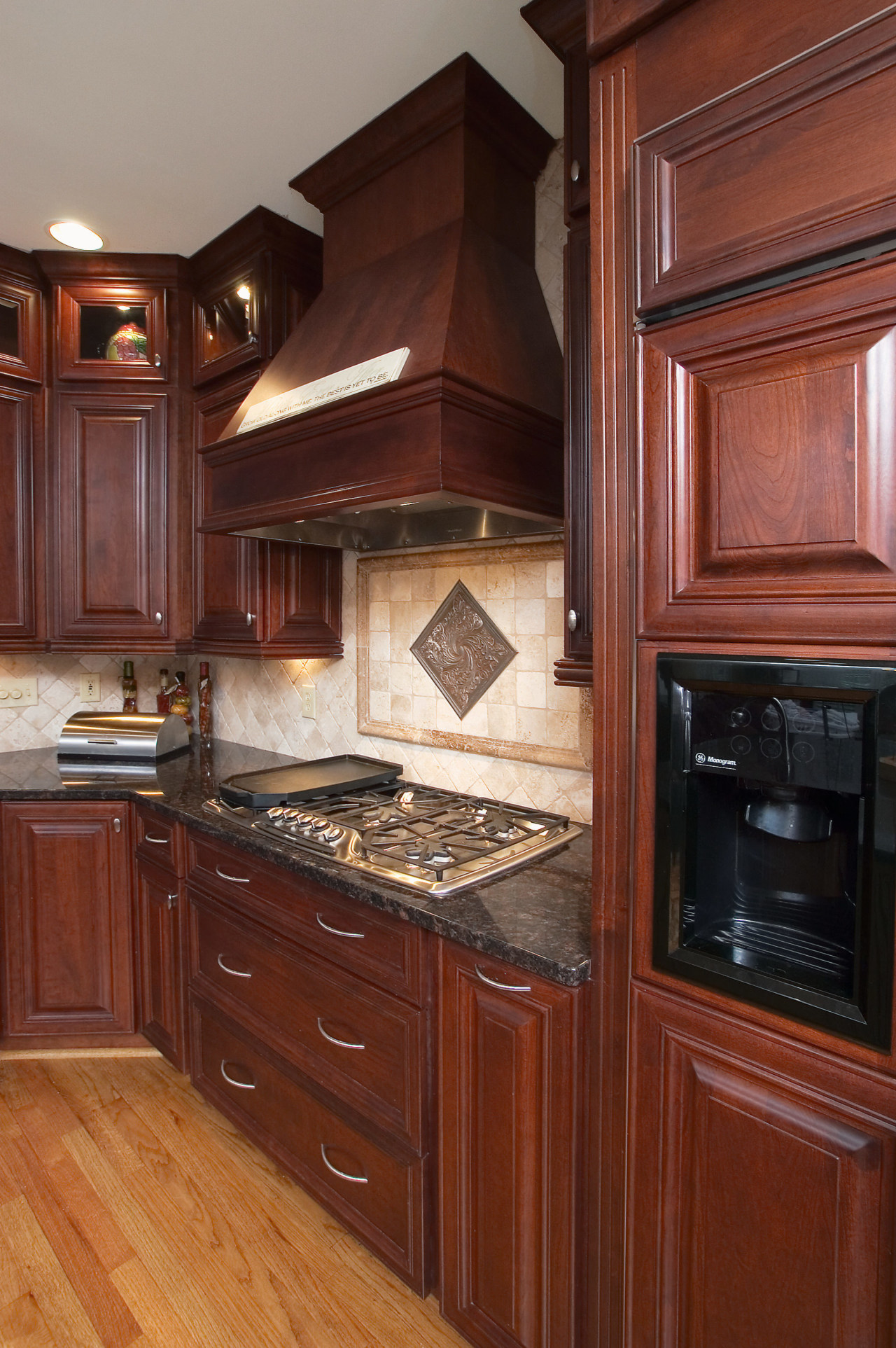 A view of this kitchen featuring custom cherry cabinetry, countertop, cuisine classique, floor, flooring, furniture, hardwood, home, home appliance, interior design, kitchen, kitchen appliance, kitchen stove, room, under cabinet lighting, wood, wood flooring, wood stain, red