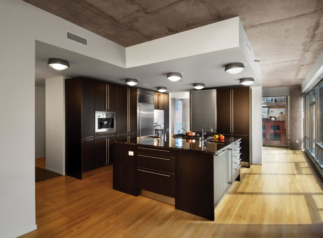 A view of an apartment complex developed by cabinetry, ceiling, countertop, floor, flooring, hardwood, interior design, kitchen, laminate flooring, wood flooring, gray