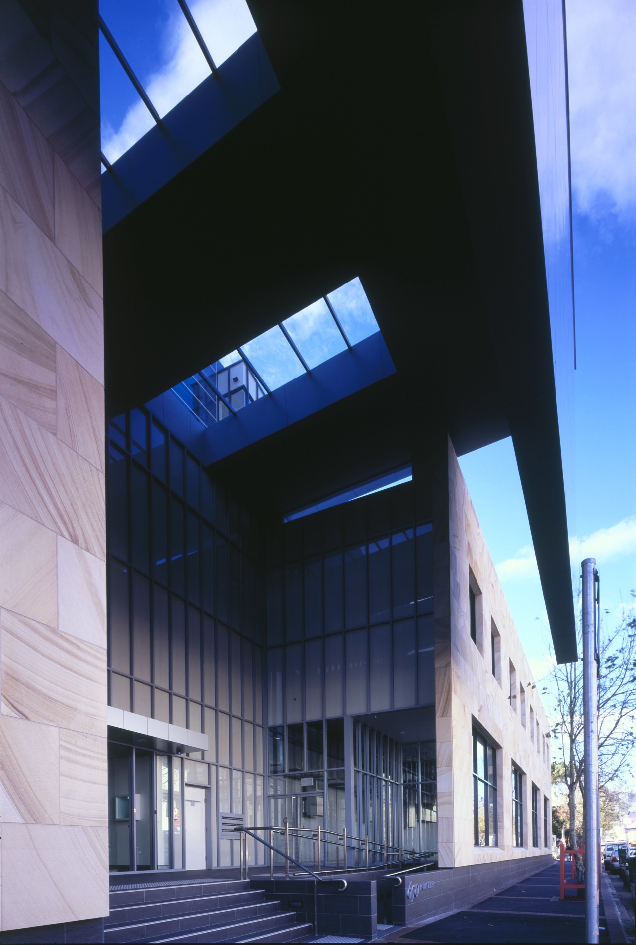 A deep overhead canopy covers the entrance to architecture, building, commercial building, corporate headquarters, daylighting, daytime, facade, glass, headquarters, house, mixed use, sky, structure, black, blue