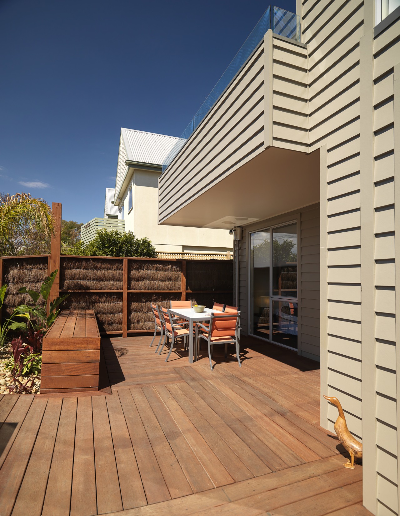 An exterior of this house featuring Merbau decking, deck, home, house, outdoor structure, real estate, residential area, siding, orange