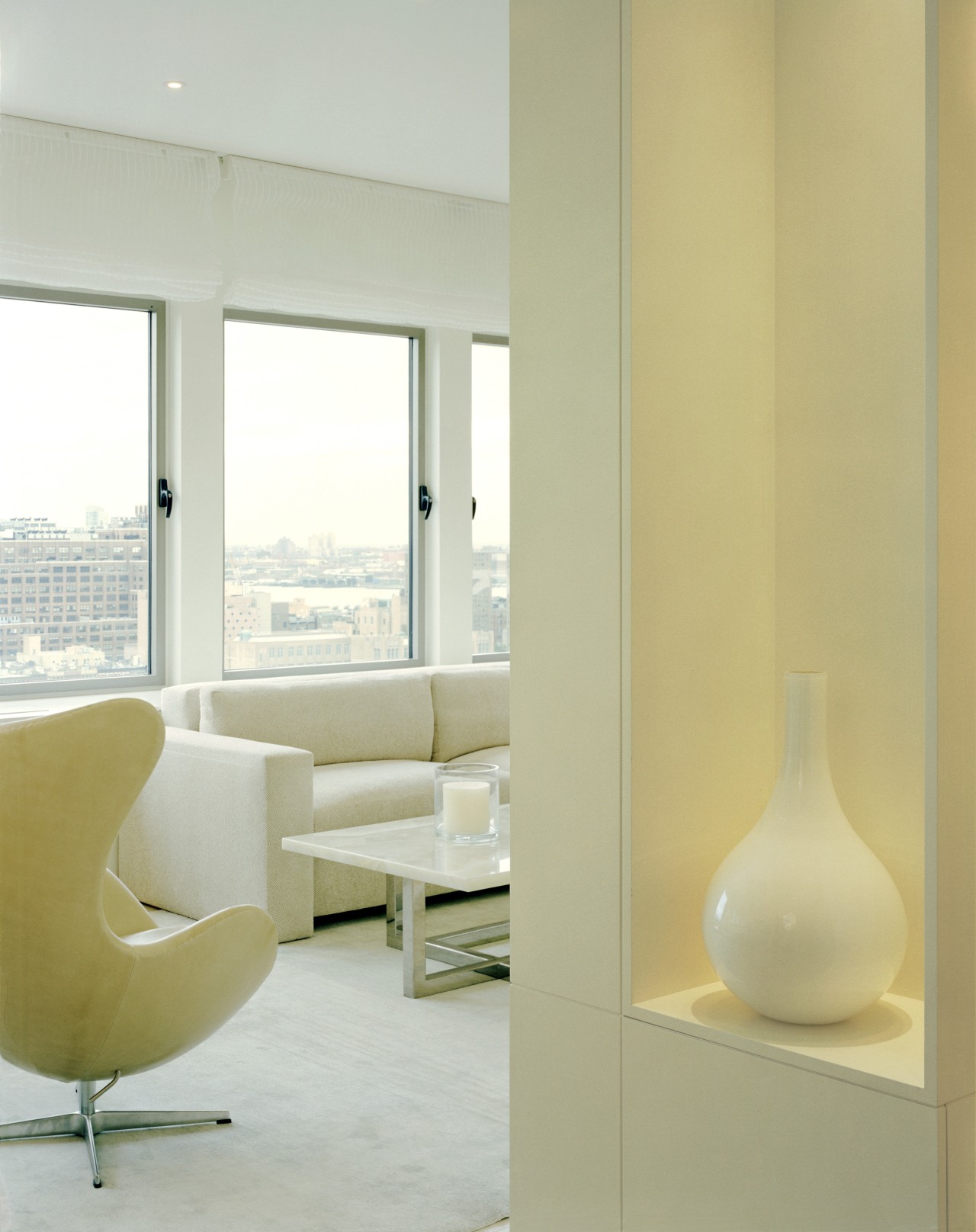 The white-on-white interior provides a tranquil refuge from floor, flooring, furniture, interior design, light fixture, lighting, living room, product design, table, wall, window, gray, orange