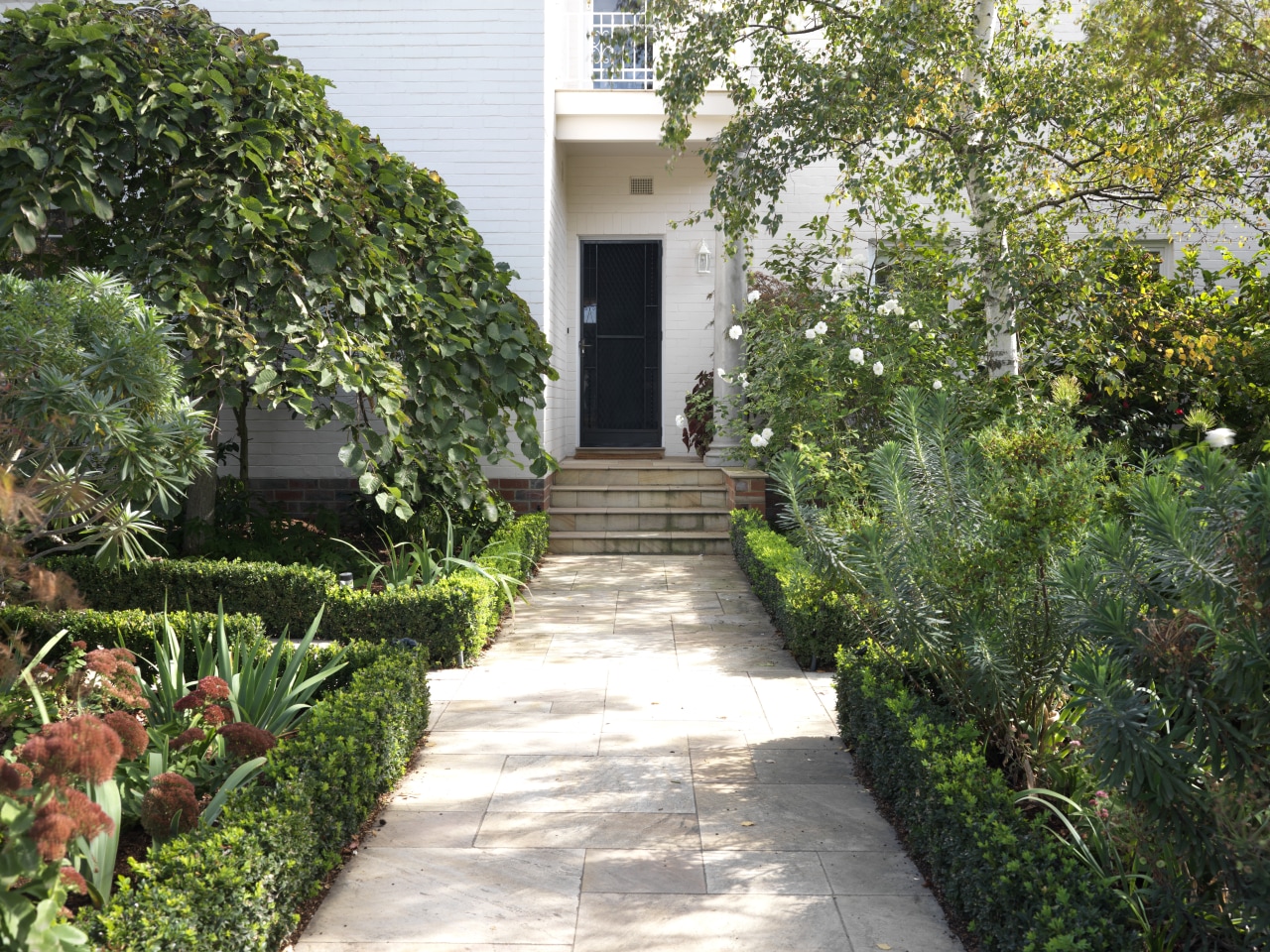 View of a landscaped garden which features a backyard, cottage, courtyard, estate, garden, grass, home, house, landscape, landscaping, lawn, leaf, outdoor structure, path, plant, property, real estate, shrub, tree, walkway, yard, green