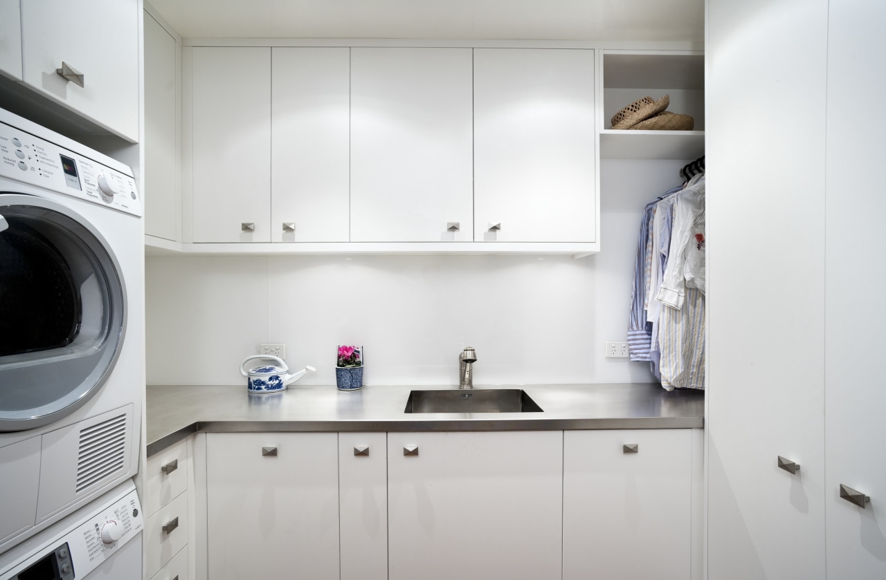 View of laundry which features white cabinetry, sink cabinetry, clothes dryer, countertop, home appliance, interior design, kitchen, laundry, laundry room, major appliance, product design, room, washing machine, gray, white