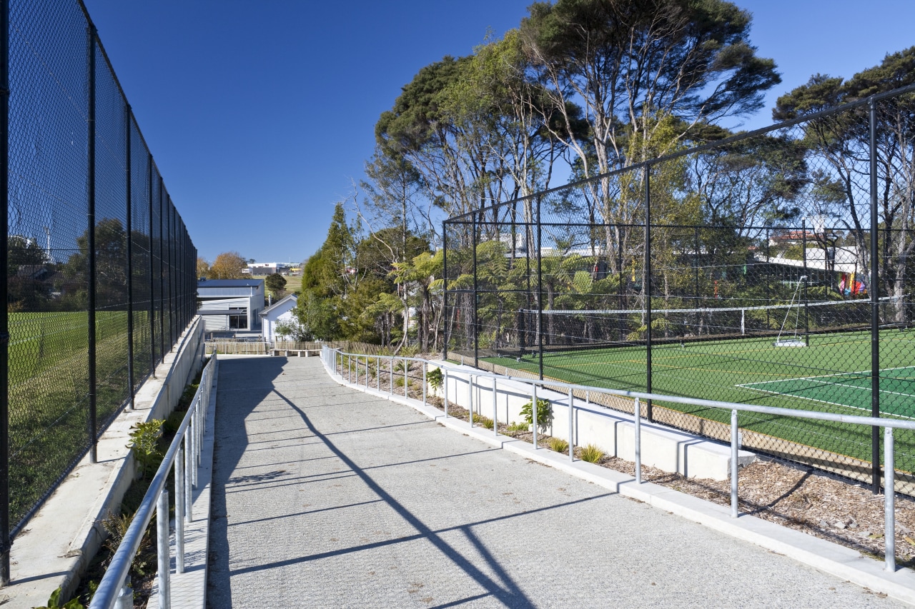Exterior view of a concrete pathway at Albany architecture, area, estate, fence, grass, house, landscape, outdoor structure, park, plant, public space, real estate, recreation, residential area, sky, sport venue, structure, tree, walkway, white
