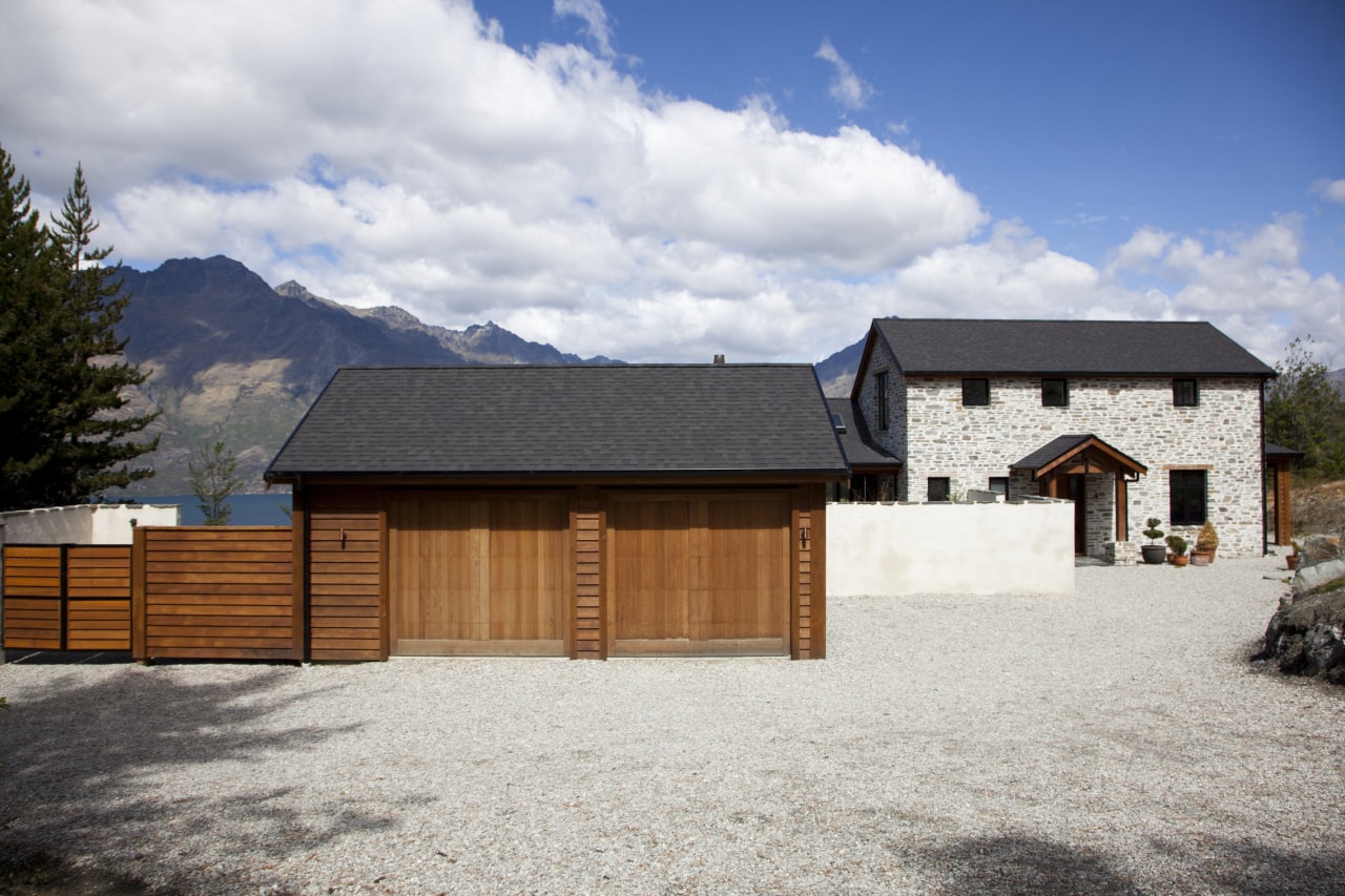 View of exterior with wooden garage in foreground barn, cottage, facade, home, house, property, real estate, roof, shed, sky, white, gray