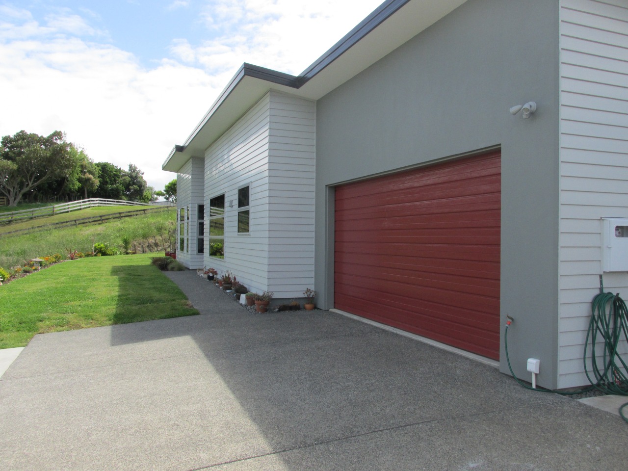 The exterior of this four-bedroom family residence designed asphalt, door, facade, garage, garage door, home, house, property, real estate, residential area, siding, window, gray