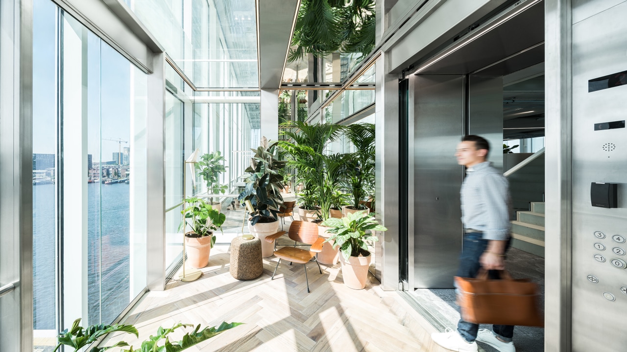 The elevator trough which visitors enter the building architecture, balcony, building, daylighting, door, facade, flowerpot, glass, home, house, houseplant, interior design, plant, property, real estate, room, window, white