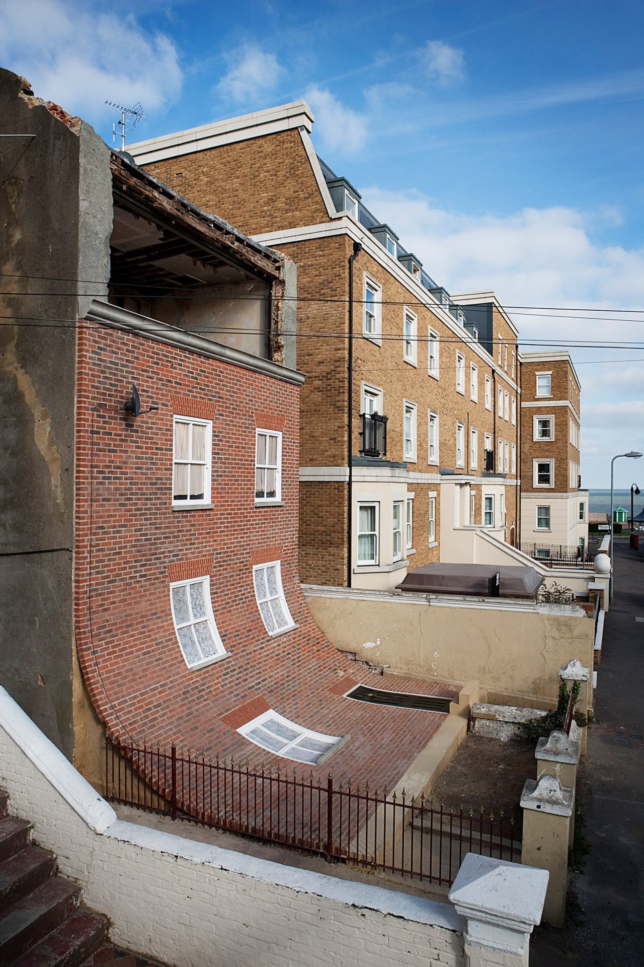 Alex Chinneck – From the knees of my apartment, architecture, blue, brick, brickwork, building, facade, home, house, neighbourhood, property, real estate, residential area, roof, street, town, urban area, wall, window, gray