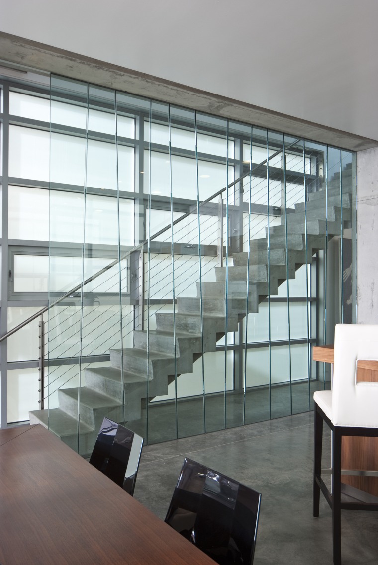 View of living space and staircase featuring vertical architecture, daylighting, glass, handrail, interior design, stairs, window, gray