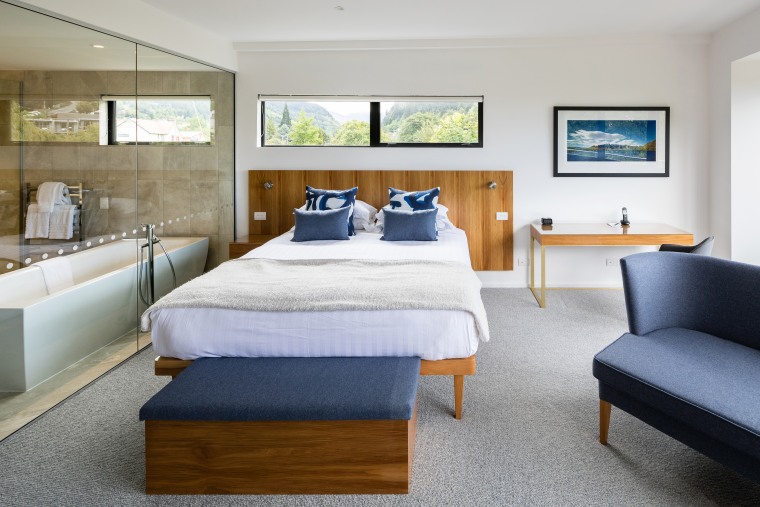 A rectangular bathtub is a modern feature within bed, bed frame, bed sheet, bedding, bedroom, boutique hotel, building, ceiling, comfort, daylighting, floor, furniture, hardwood, home, house, interior design, mattress, mattress pad, nightstand, property, real estate, room, suite, table, wall, gray