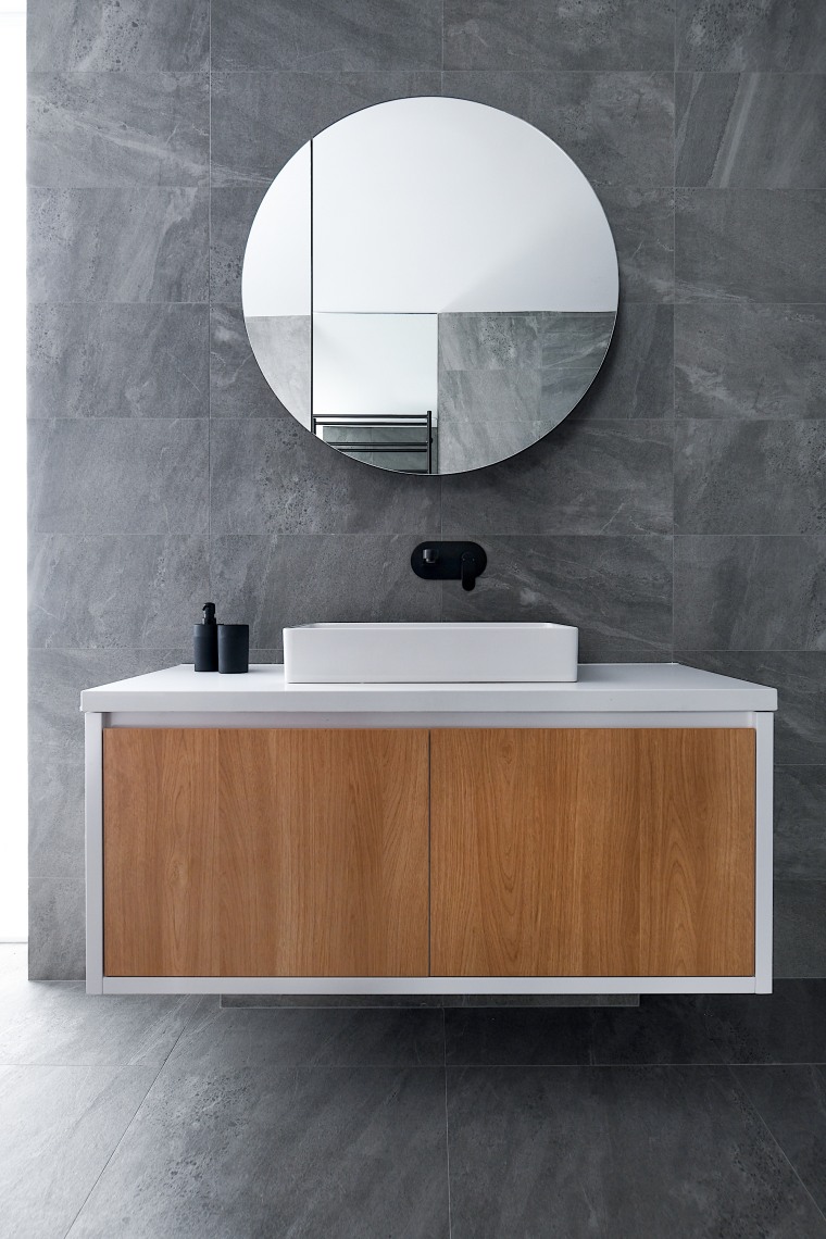 A cantilevered, clean-lined vanity cabinet and accompanying round architecture, bathroom, bathroom accessory, bathroom cabinet, ceramic, chest of drawers, floor, flooring, furniture, interior design, material property, mirror, room, sink, tap, tile, wall, wood, gray