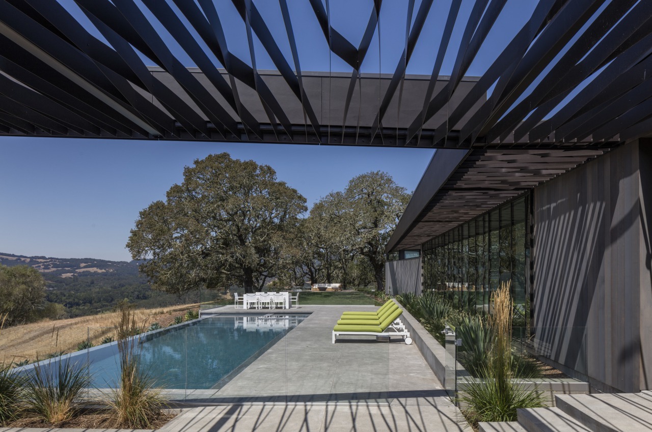 While the trellis running alongside the two wings architecture, estate, home, house, landscape, outdoor structure, plant, property, real estate, roof, sky, black