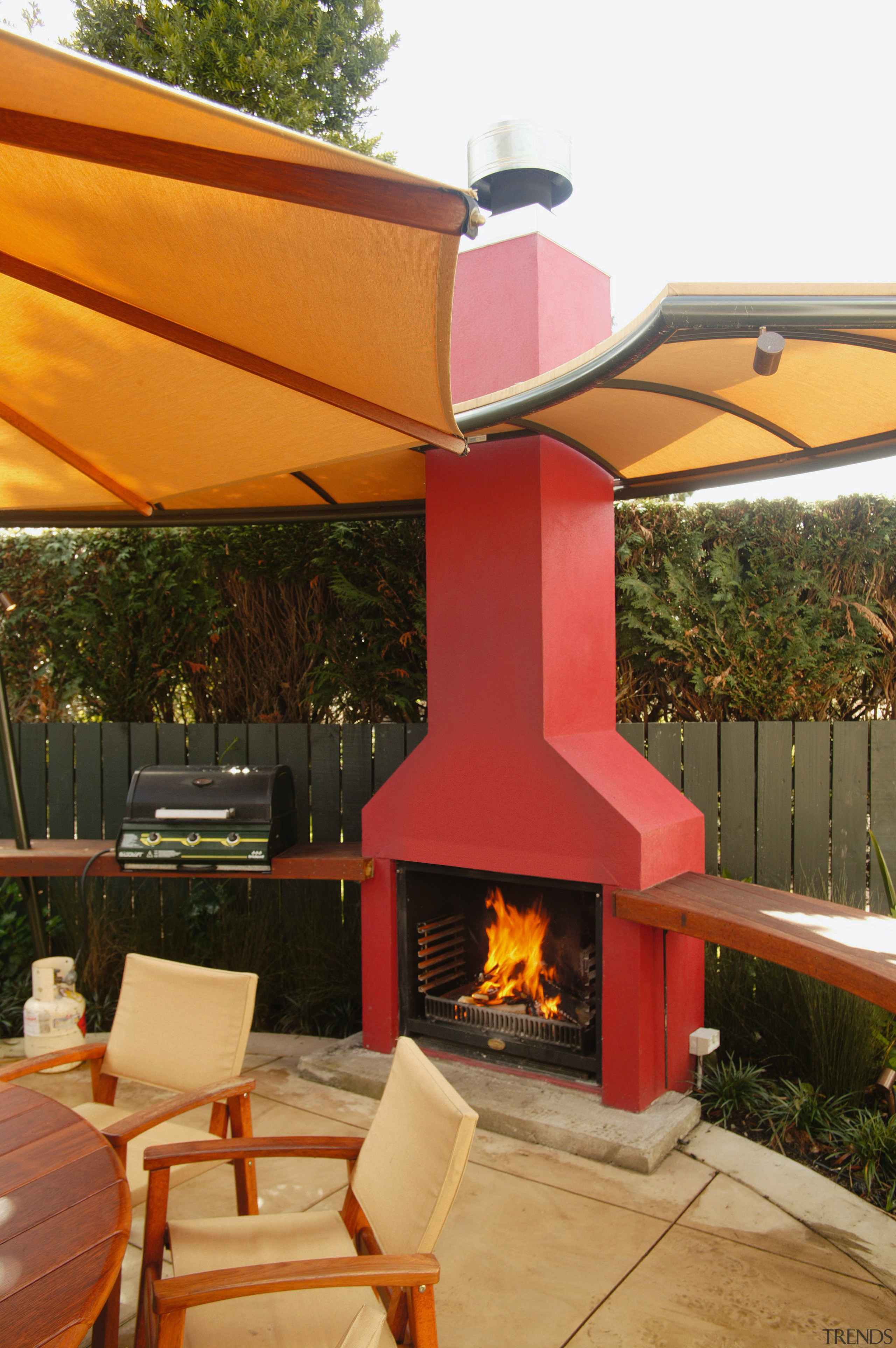 Outdoor living area with red open fireplace and backyard, home, outdoor structure, patio, brown, orange