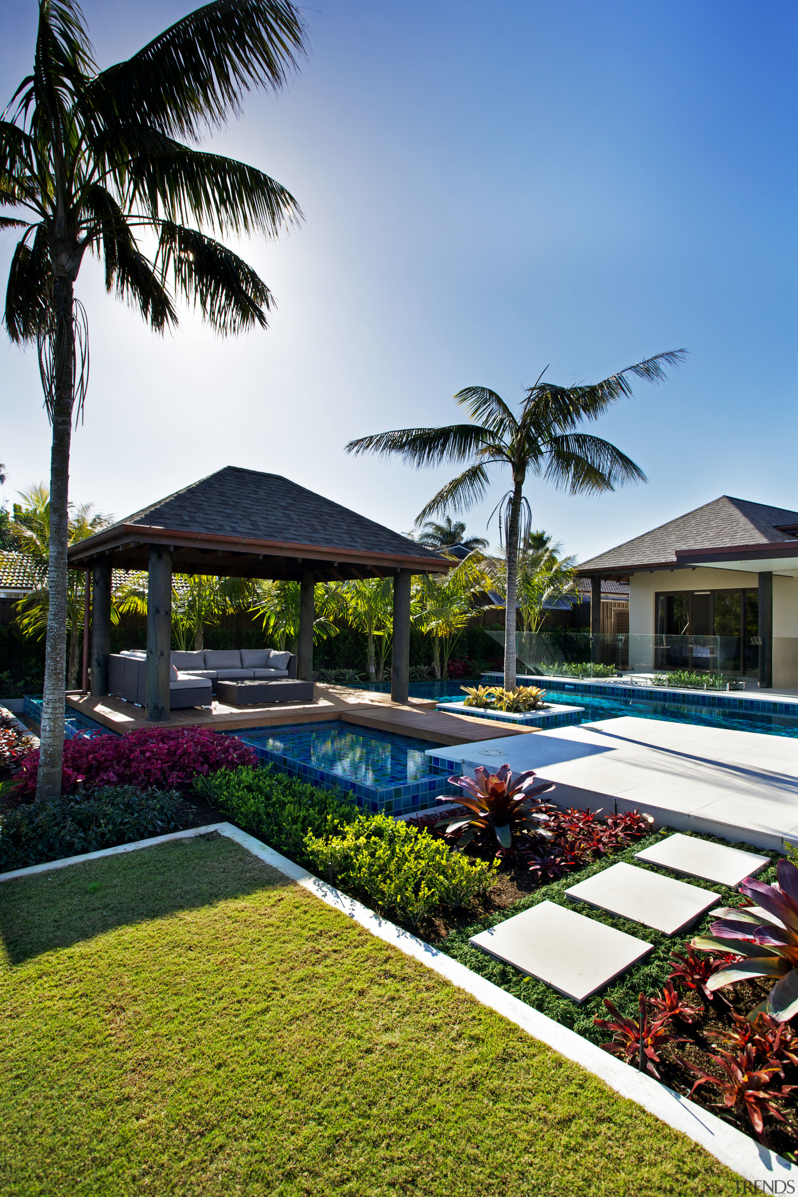 In this tropical-themed pool environment, sandstone paving and arecales, estate, home, house, leisure, palm tree, plant, property, real estate, resort, swimming pool, tree, villa